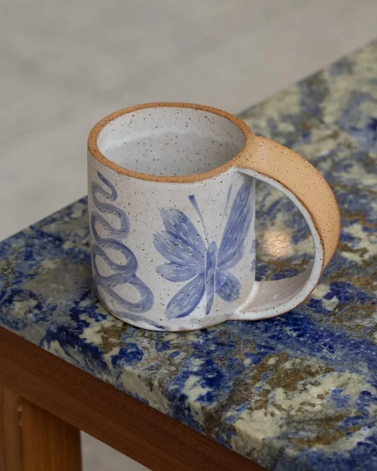 Decorative ceramic mug with a blue butterfly design on a blue and brown speckled granite countertop.