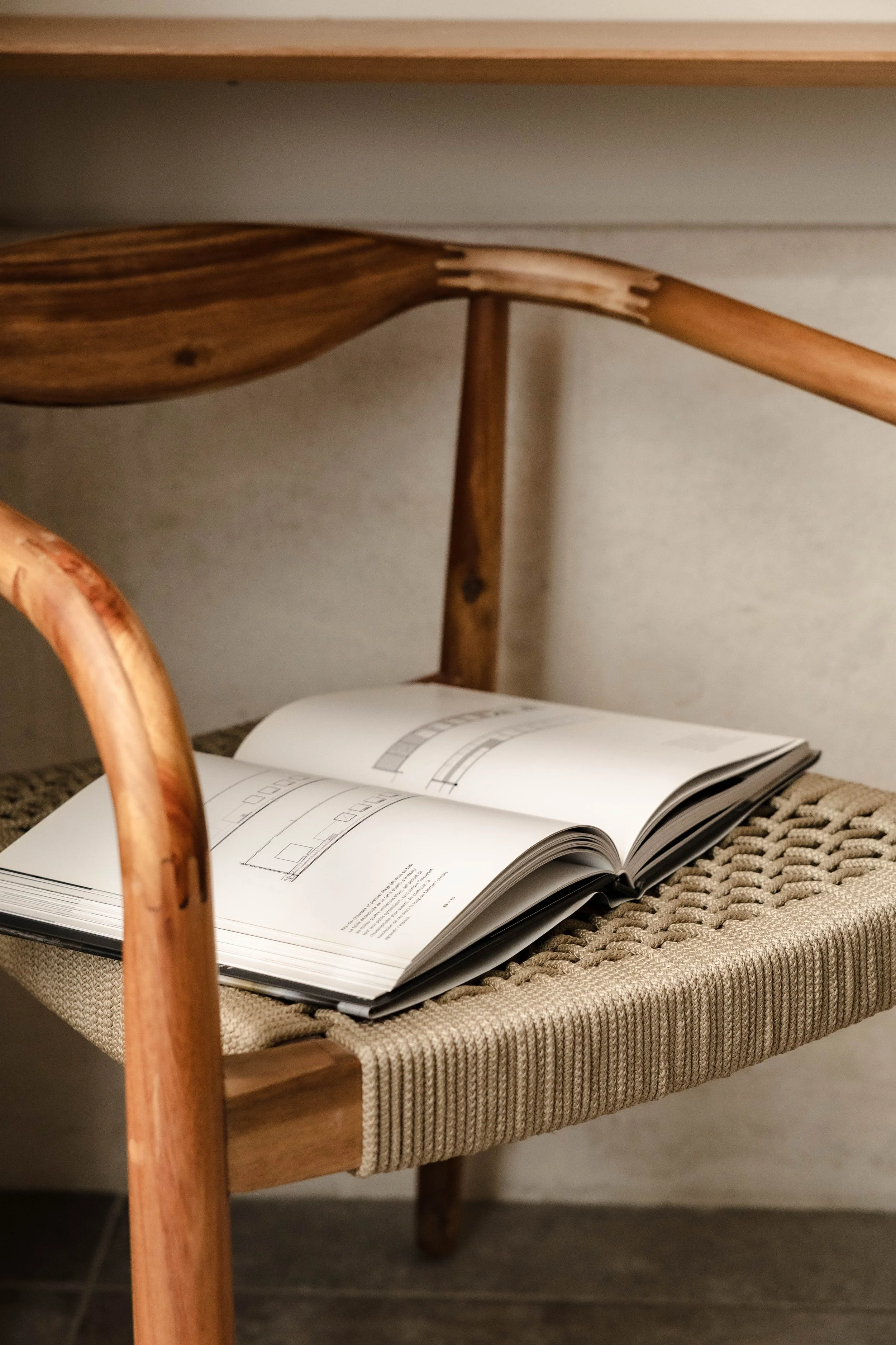 Wooden chair with woven seat and open book of architectural drawings resting on it.