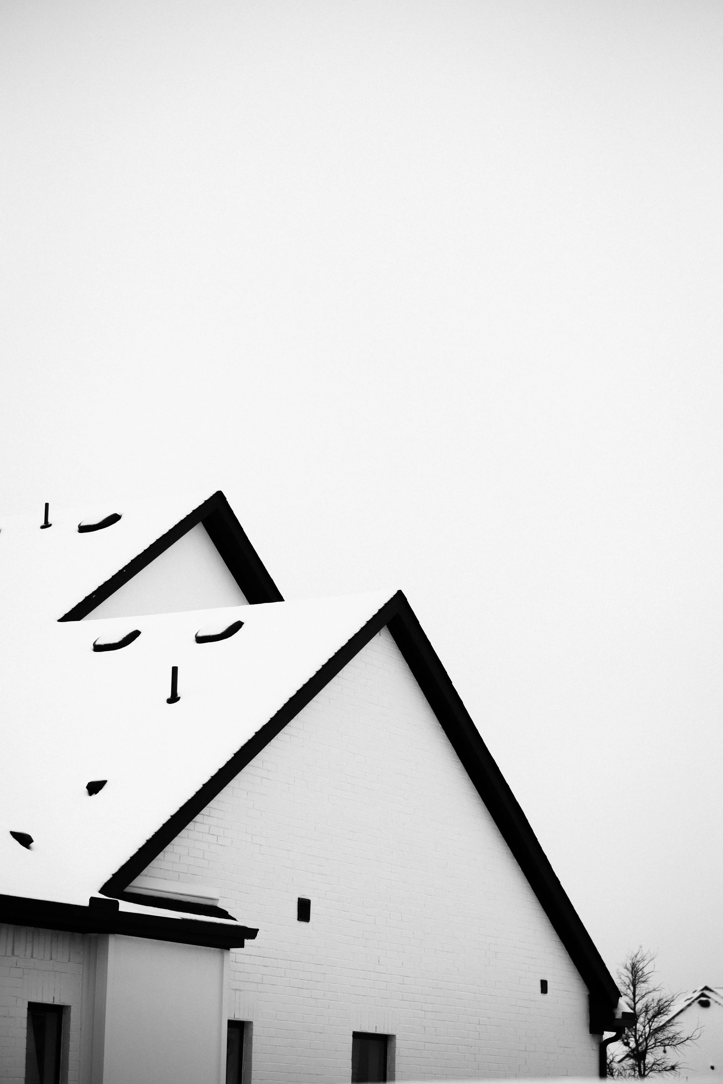Black and white photo of a church with a steep roof, snow on the roof, and three windows on the side wall.
