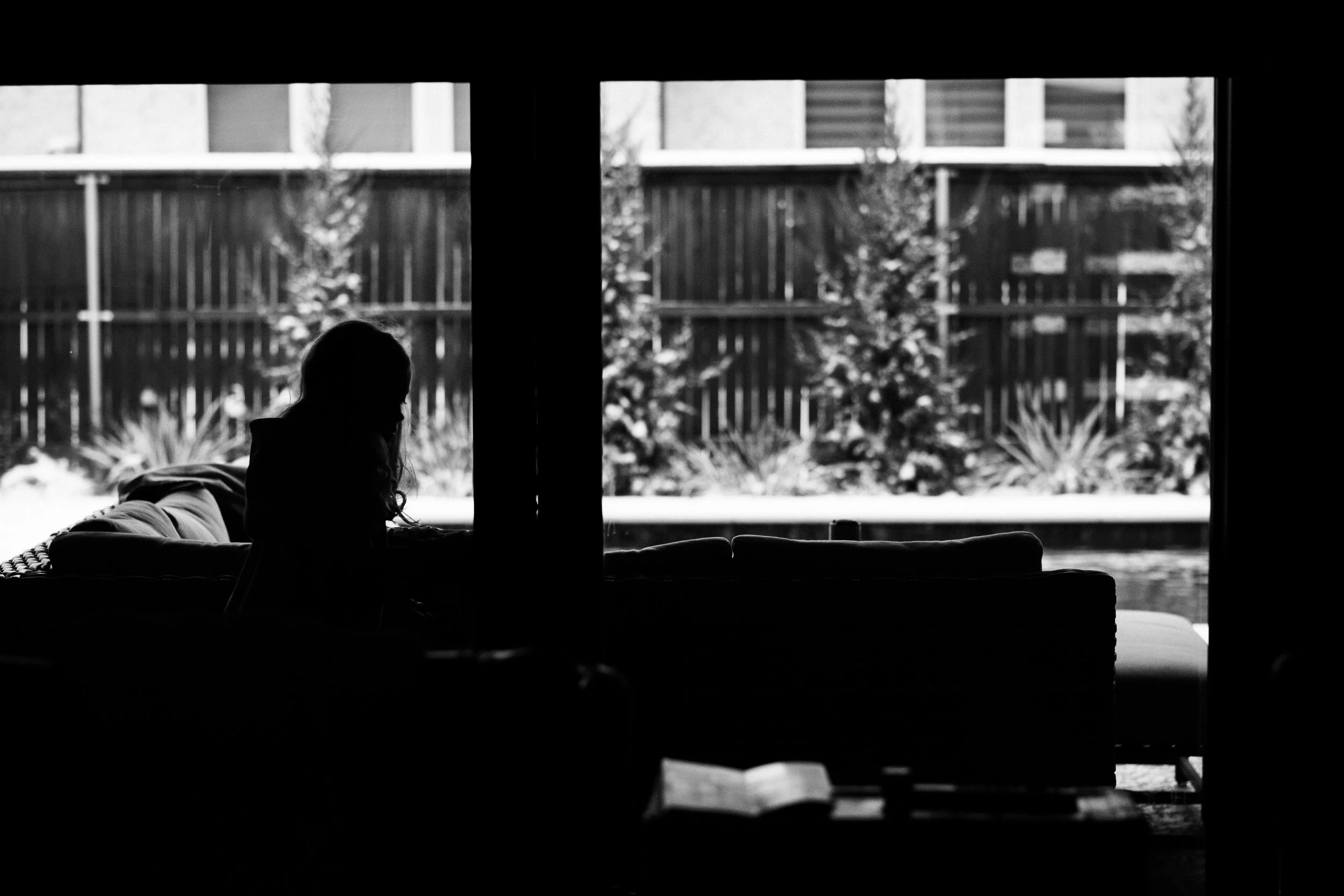Silhouette of a person sitting on a sofa near a large window with a garden outside.