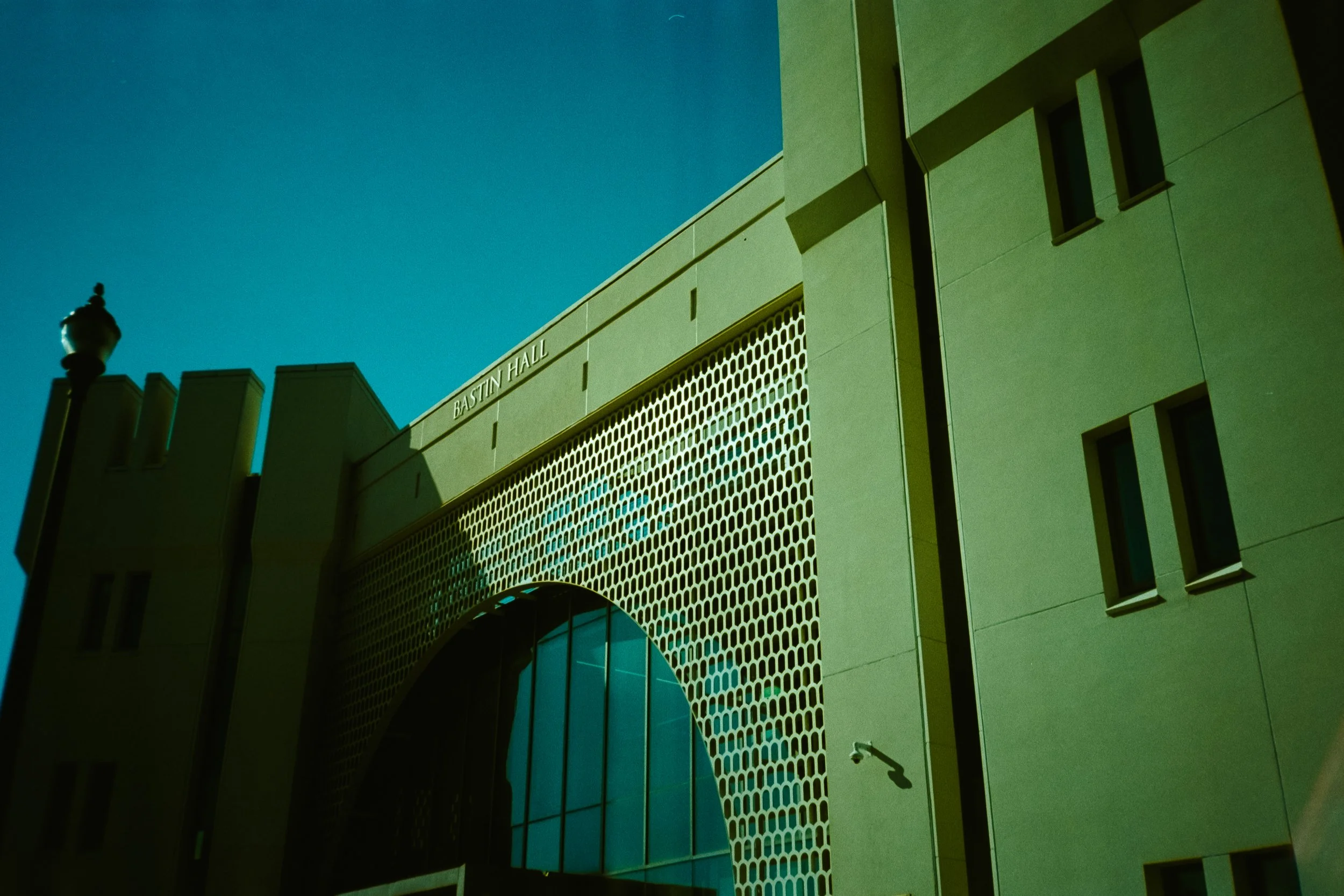 Exterior view of Bastin Hall building with modern architectural design, including geometric patterns on the facade, small windows, and a streetlamp in the foreground, under a clear blue sky.