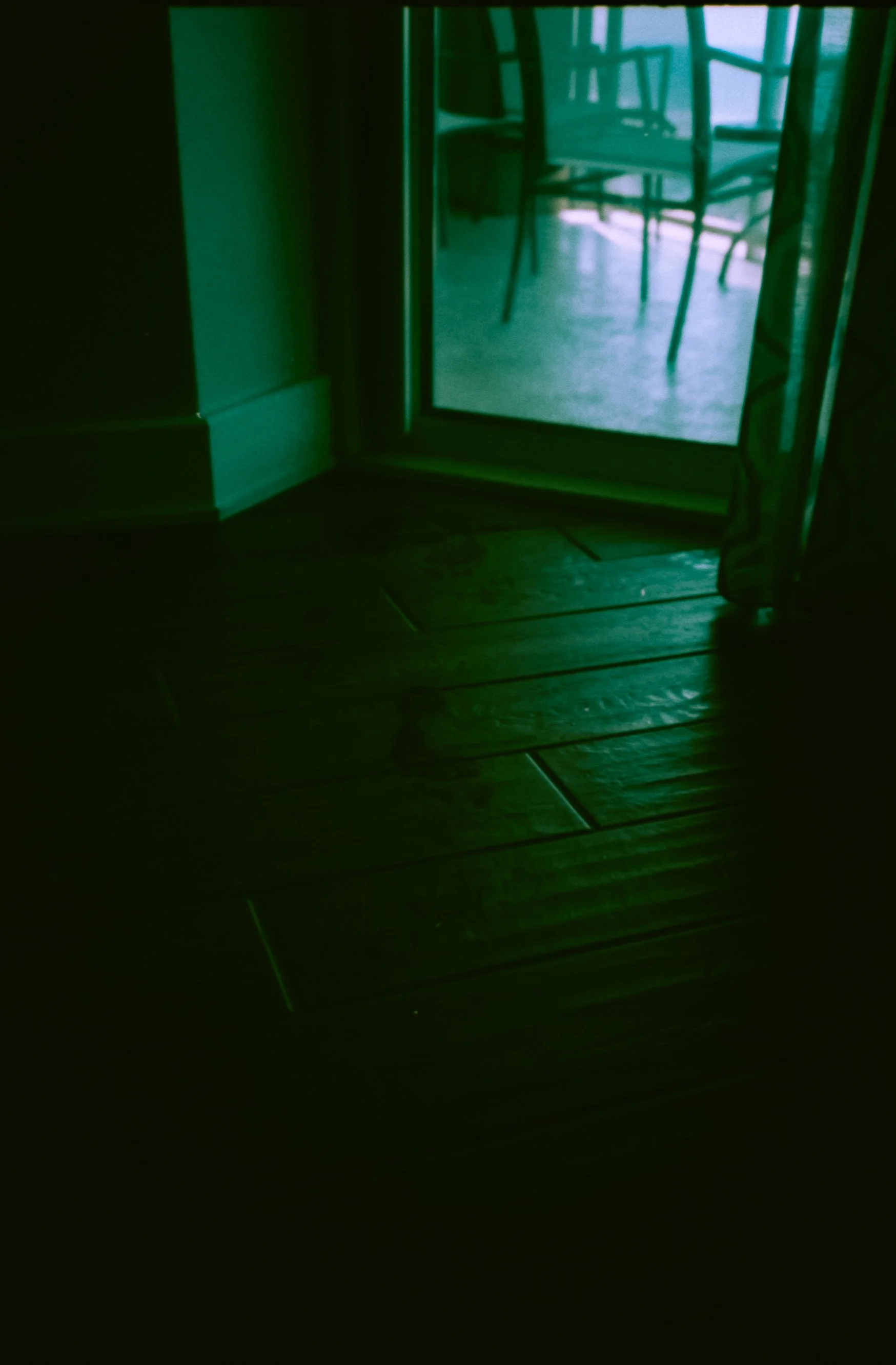 View of chairs through glass door with green tint, with green-hued wooden floor in foreground.