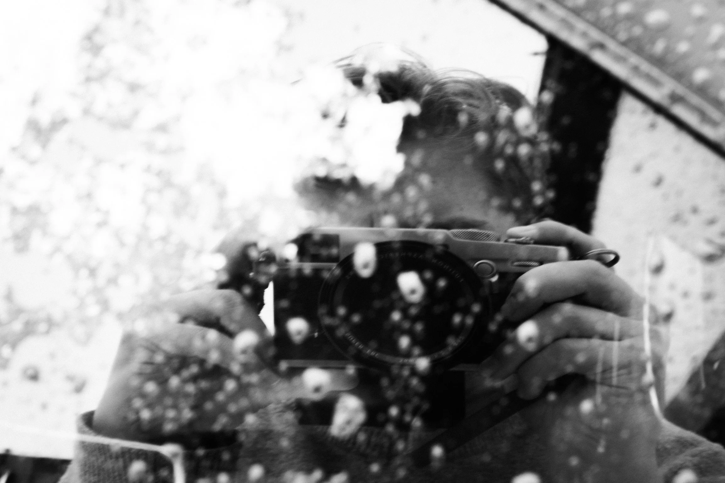 A person taking a self-portrait with a camera, with snow on the mirror and in the background. The image is in black and white.