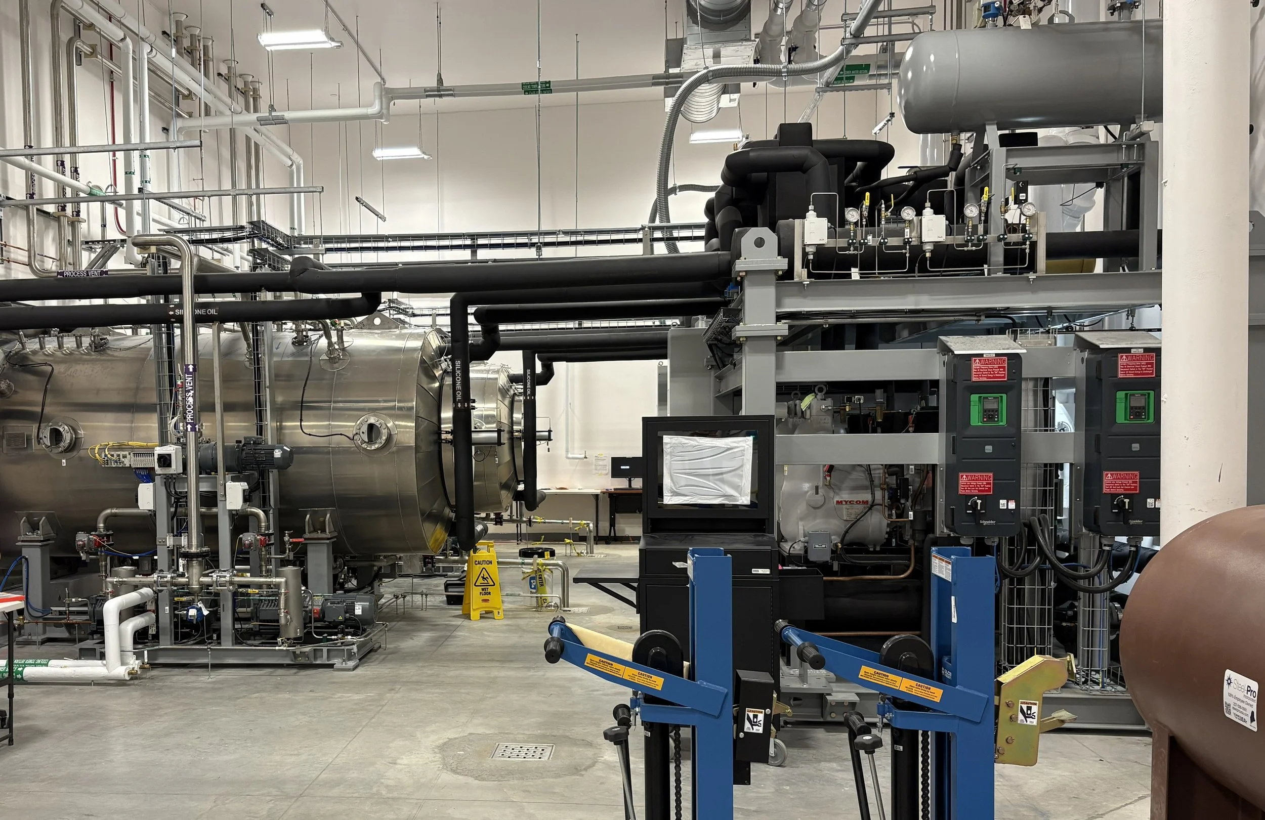 Industrial machinery and equipment in a plant or factory setting, including pipes, gauges, control panels, and warning signs.