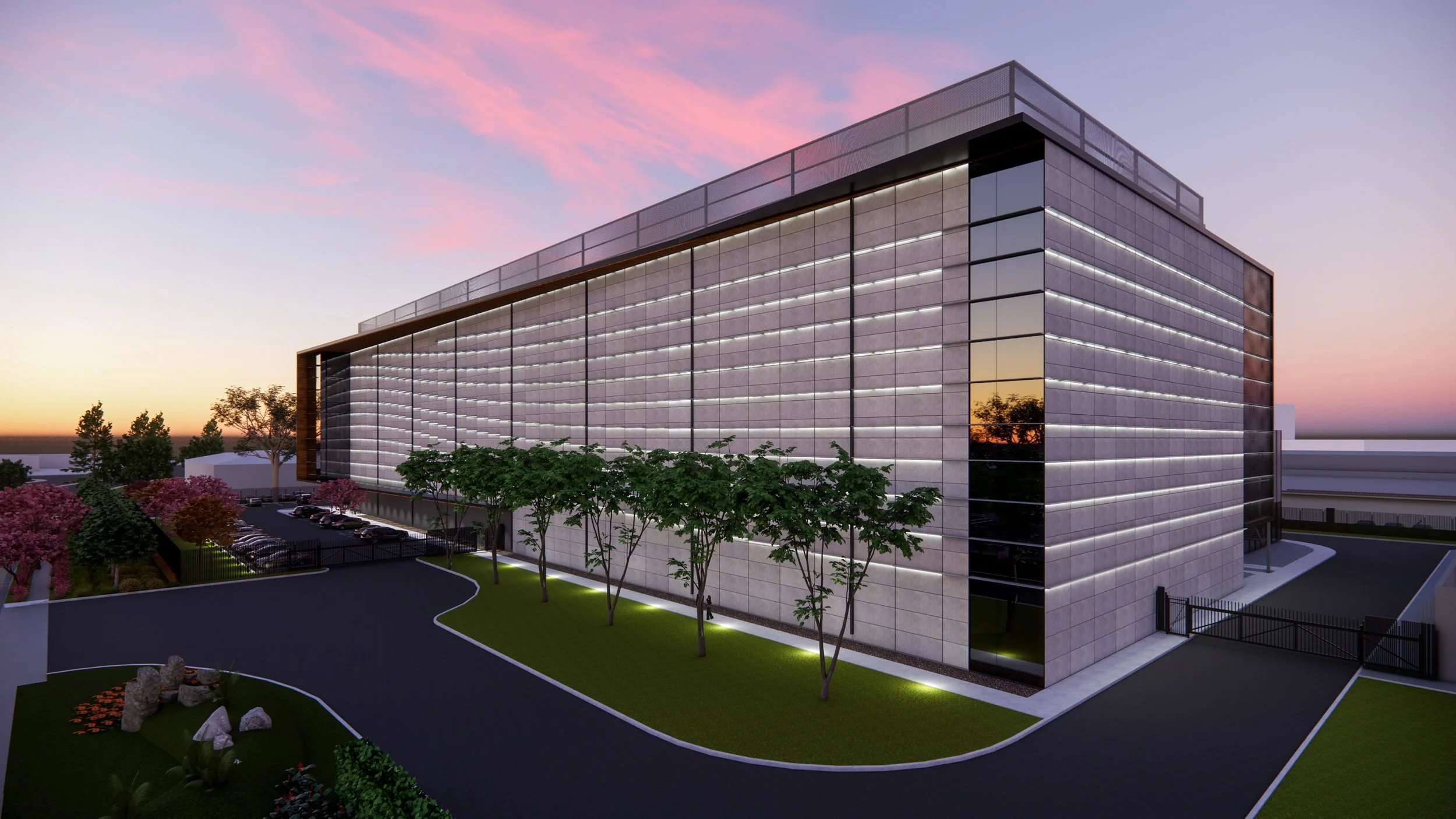 Modern multi-story office building with glass and metal facade, surrounded by landscaped greenery and parking lot, during sunset with pink and purple sky.