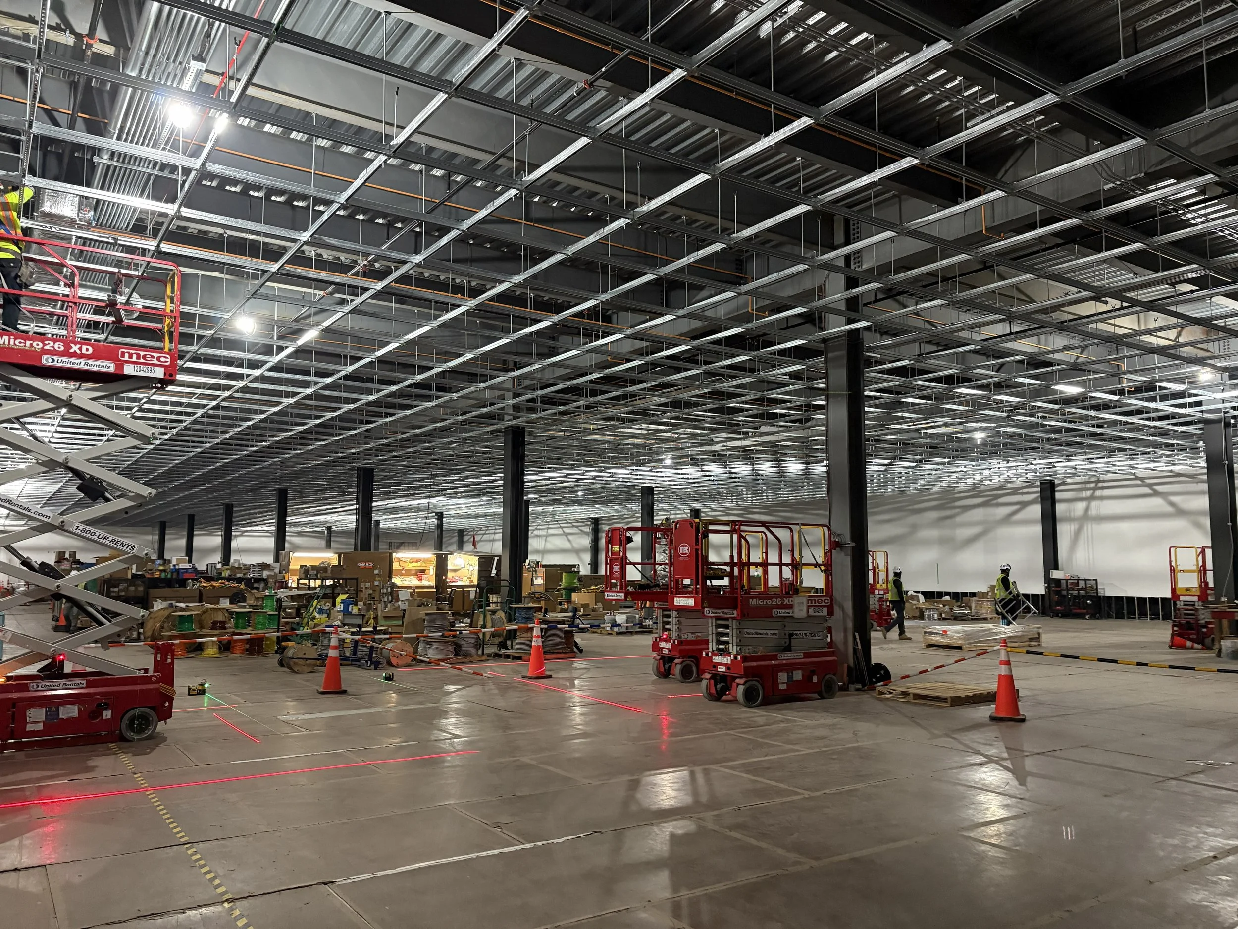 Interior construction site with exposed ceiling framework, construction equipment, tools, and workers wearing safety gear.