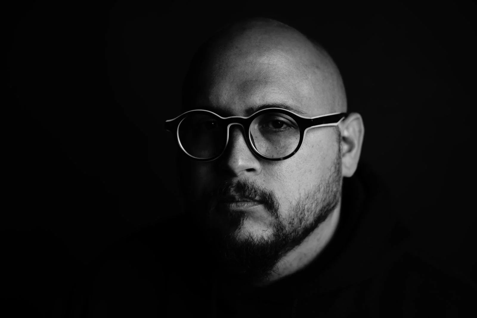 Black and white portrait of a man with glasses and a beard, looking straight at the camera with a serious expression.