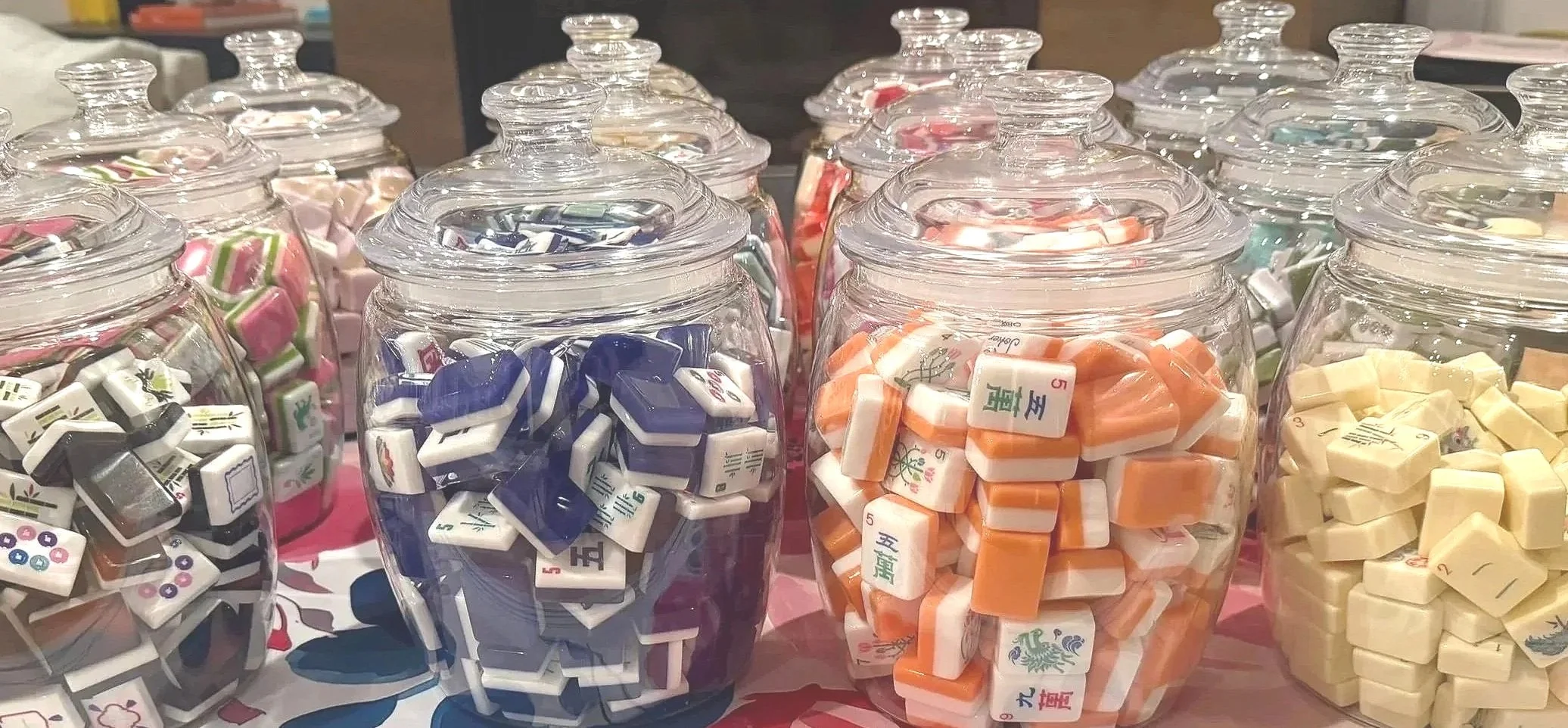 Multiple glass jars filled with colorful Mahjong tiles, arranged on a table.