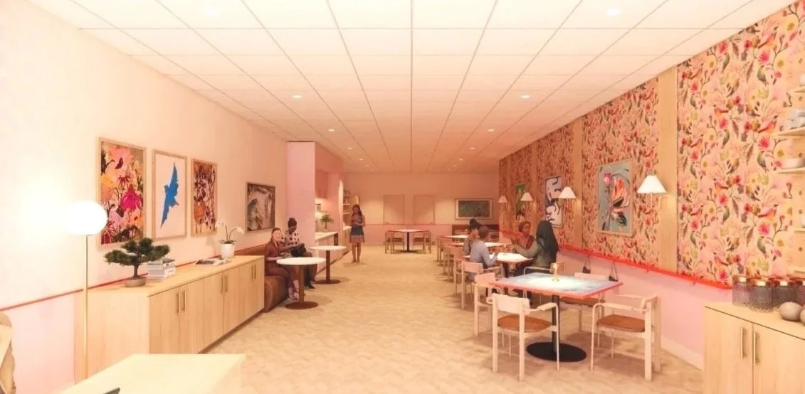 Interior of One Bam Bird's space, with pink and floral wallpaper walls, wooden furniture, and artwork on the walls. Several people are sitting at tables and a few are standing.