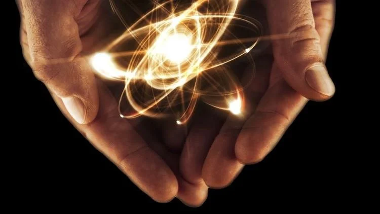 Two hands holding a glowing, swirling atom-like light with bright streaks against a dark background.