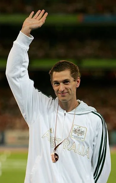 A male athlete in an Australia jacket waving at a sporting event.