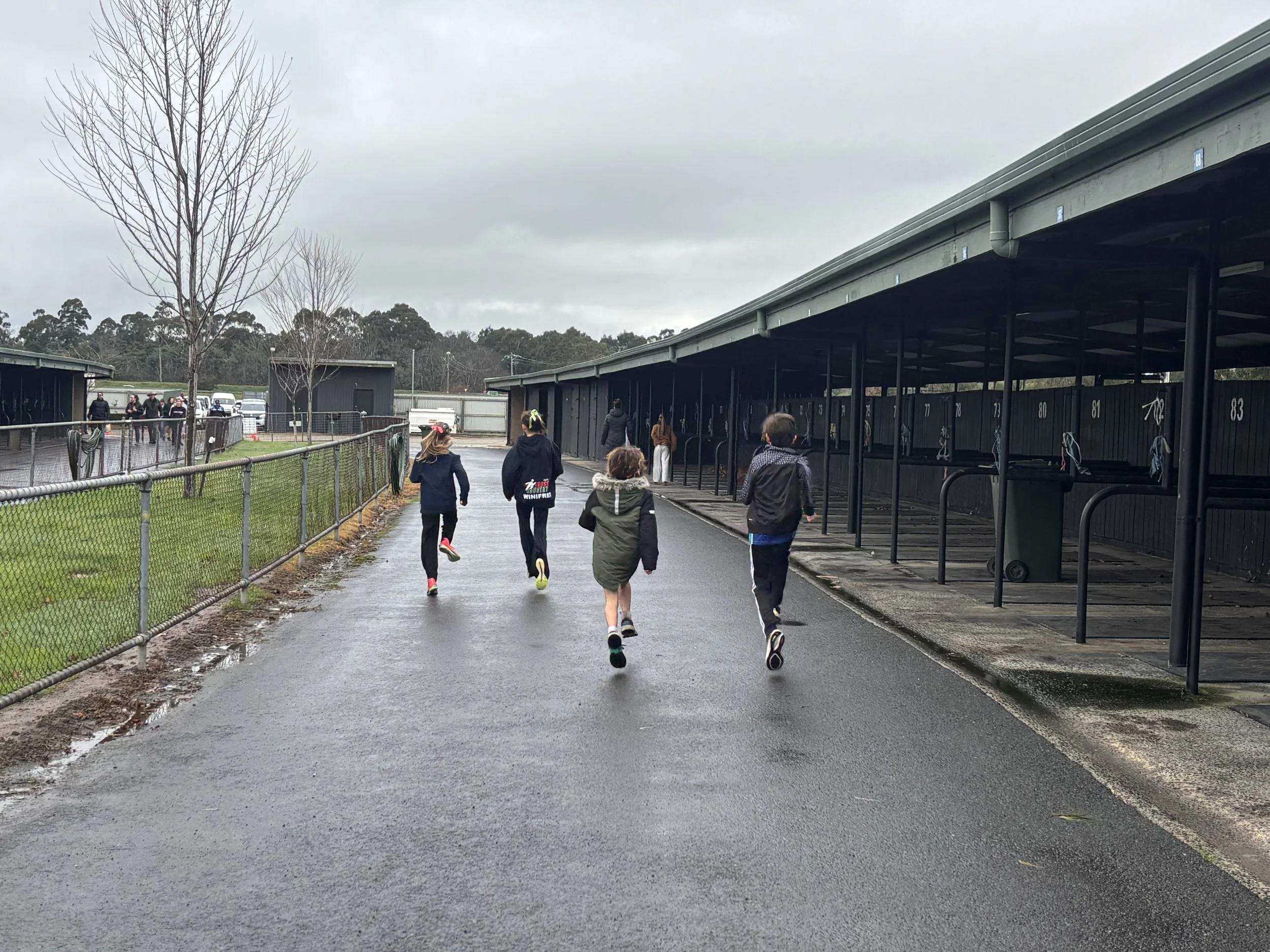 People walking on a wet pathway outside near a fenced area and storage units under an overcast sky.