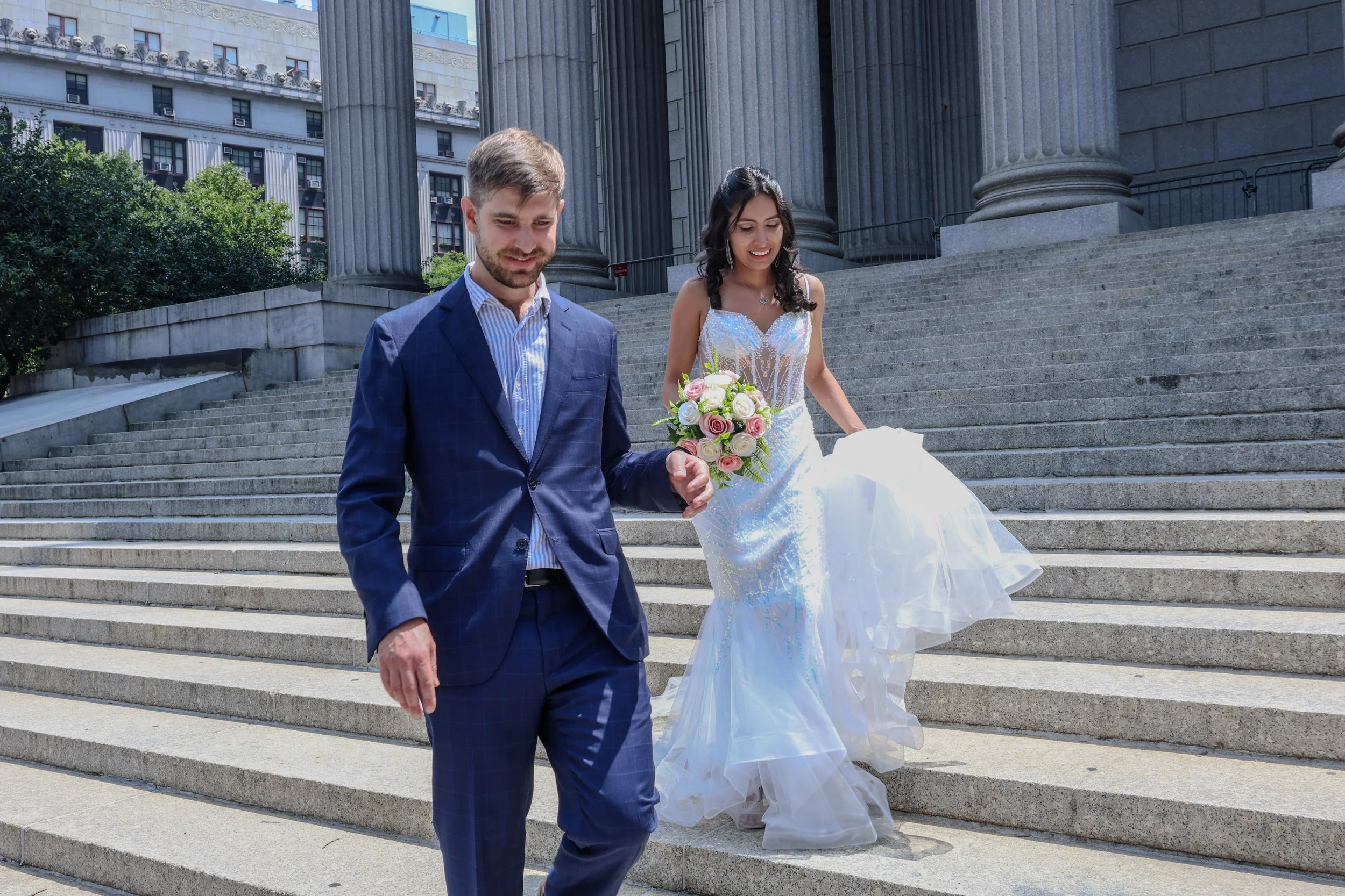 A bride and groom walking down the steps outside a government building with columns, during a wedding ceremony.
