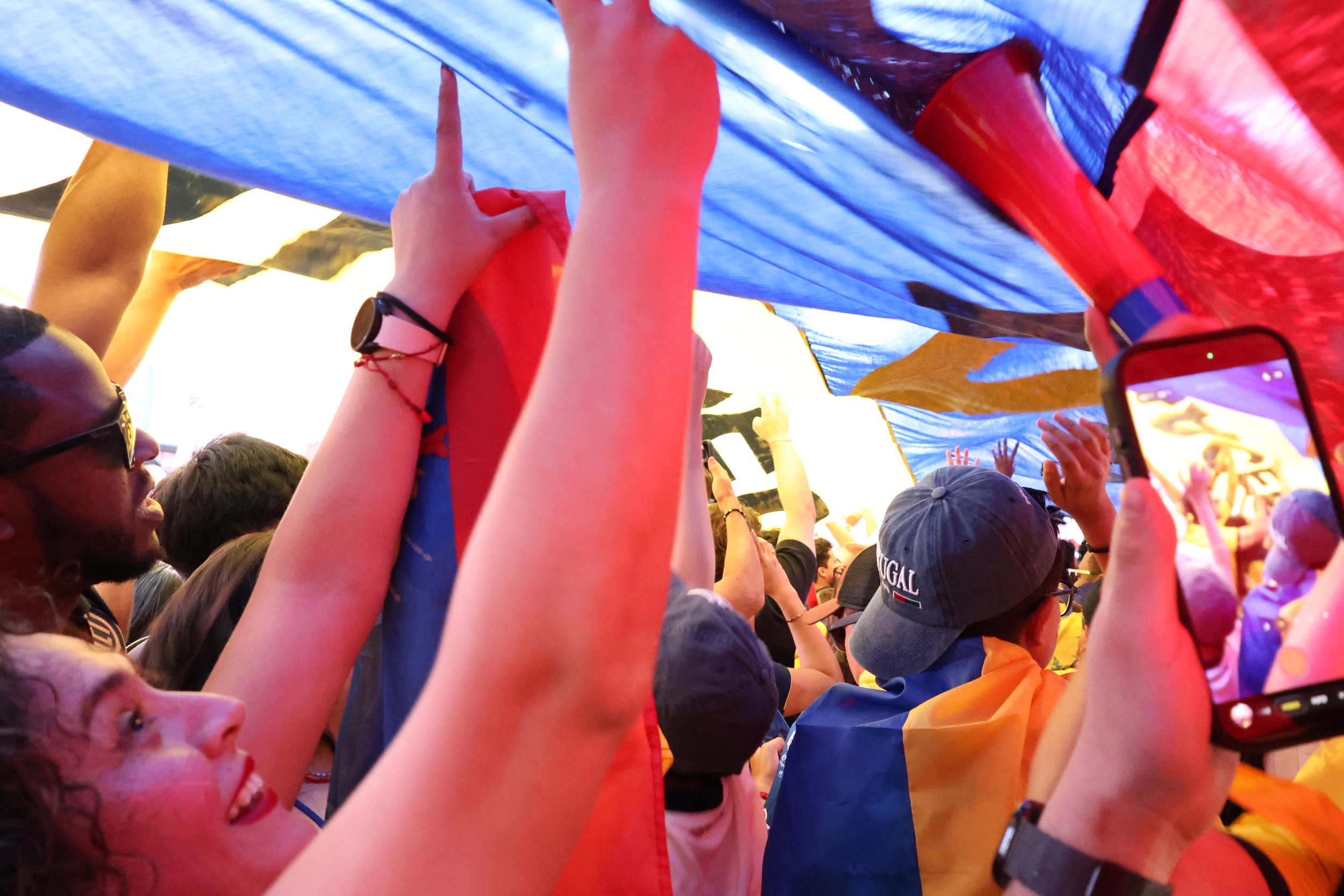 People gathered at a celebration holding a large multi-colored flag overhead.