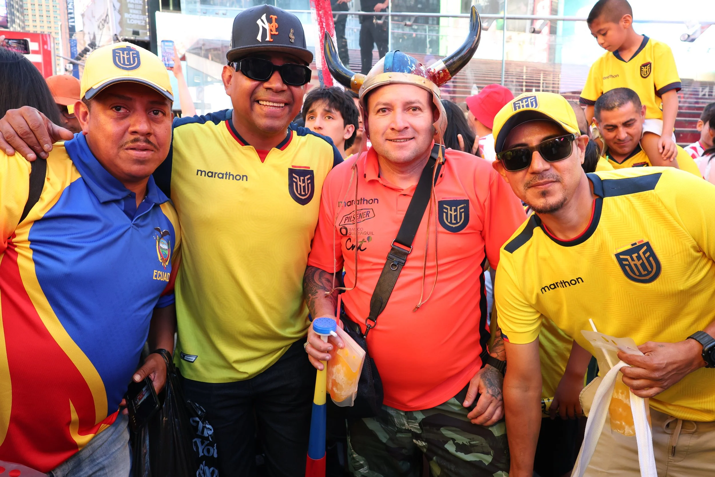 A group of men and children wearing yellow Ecuador national football team jerseys, some with sunglasses, posing for a photo in a crowded outdoor area.
