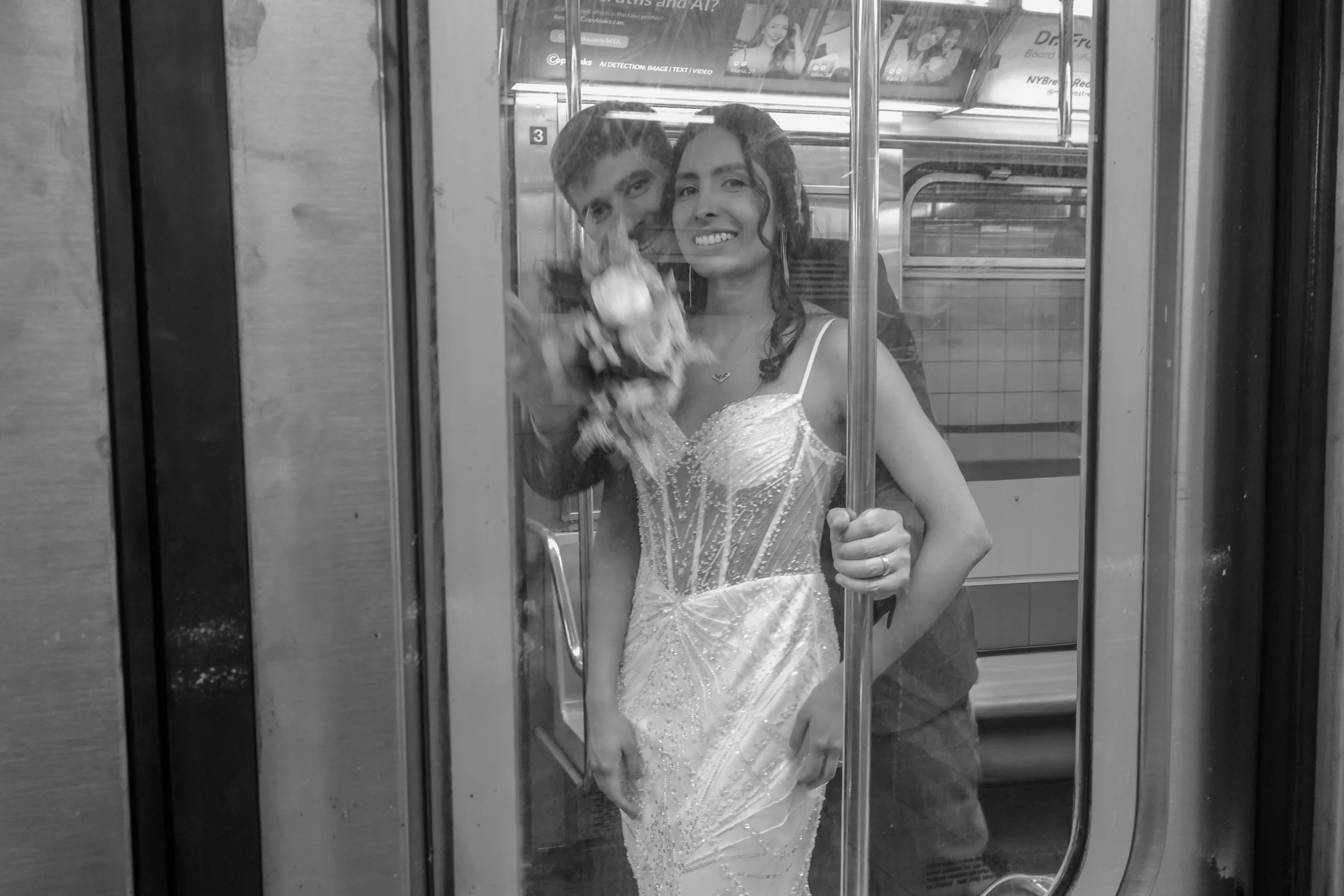 A young woman in an embellished dress holding an umbrella, looking at her reflection in an elevator mirror, with a young man partially visible behind her.