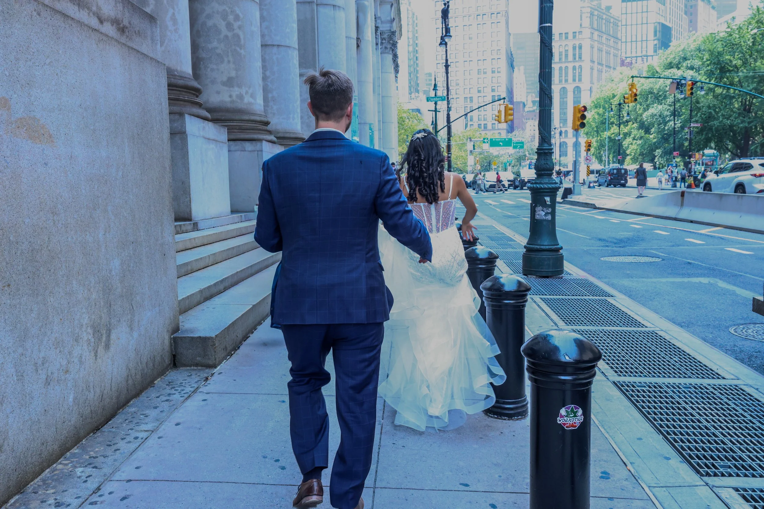 A man and woman walking together on a city sidewalk near large buildings and traffic lights.