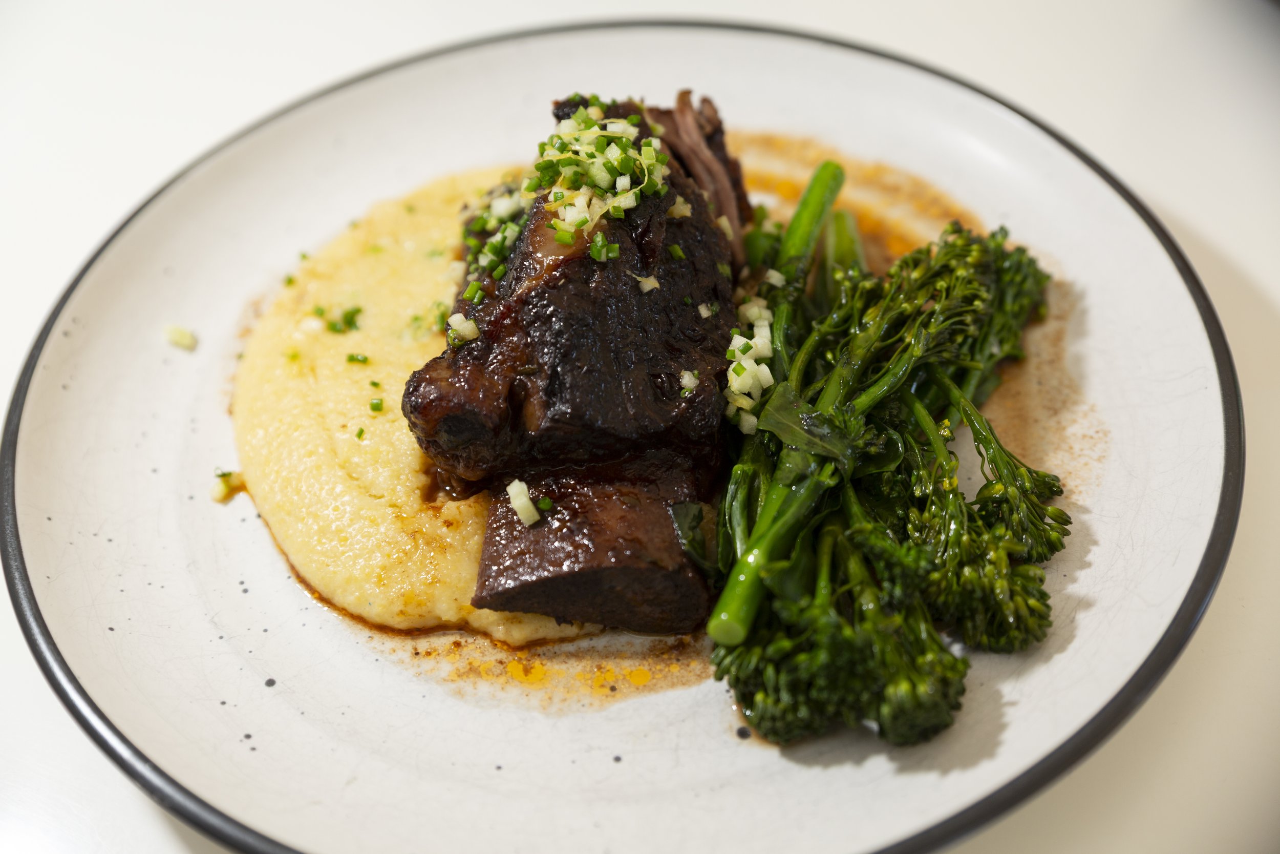 Beef rib, on a bed of orange scented polenta, beside broccolini with lemon panko crumb, and chive gremmolata. 