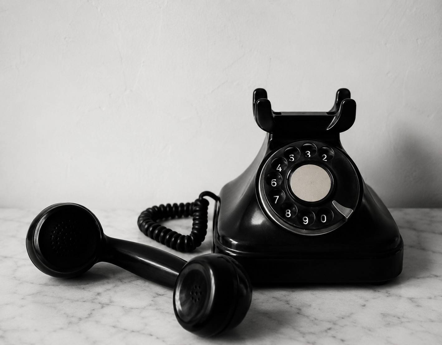 Black vintage rotary telephone with receiver on a marble surface.