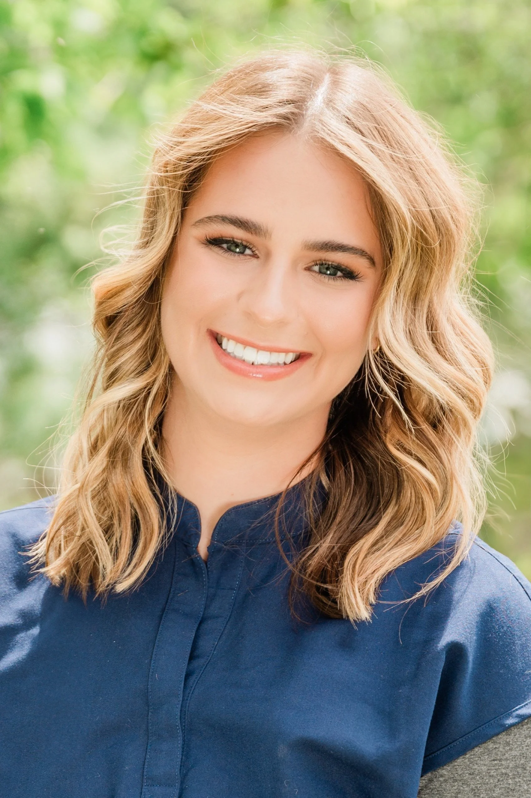 A woman with shoulder-length wavy blonde hair and blue eyes smiling outdoors, wearing a blue collared shirt. This is Danielle, a Dental Hygienist at Legacy Family Dental in Eagle River, Wisconsin.