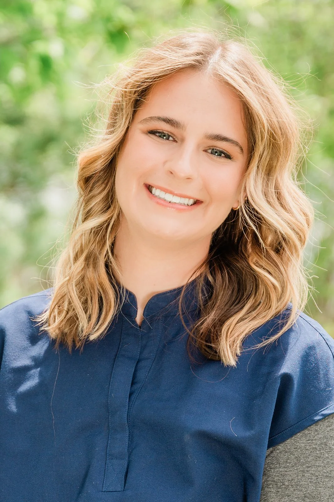 A woman with shoulder-length wavy blonde hair and blue eyes smiling outdoors, wearing a blue collared shirt. This is Danielle, a Dental Hygienist at Legacy Family Dental in Eagle River, Wisconsin.