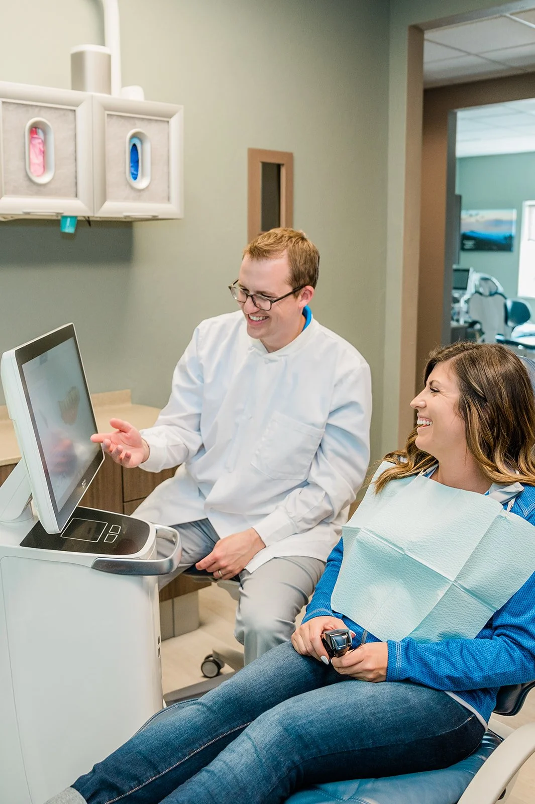 A female patient in a dental chair with a dental bib, smiling and talking to Dr. Brad Camp in the Legacy Family Dental office.