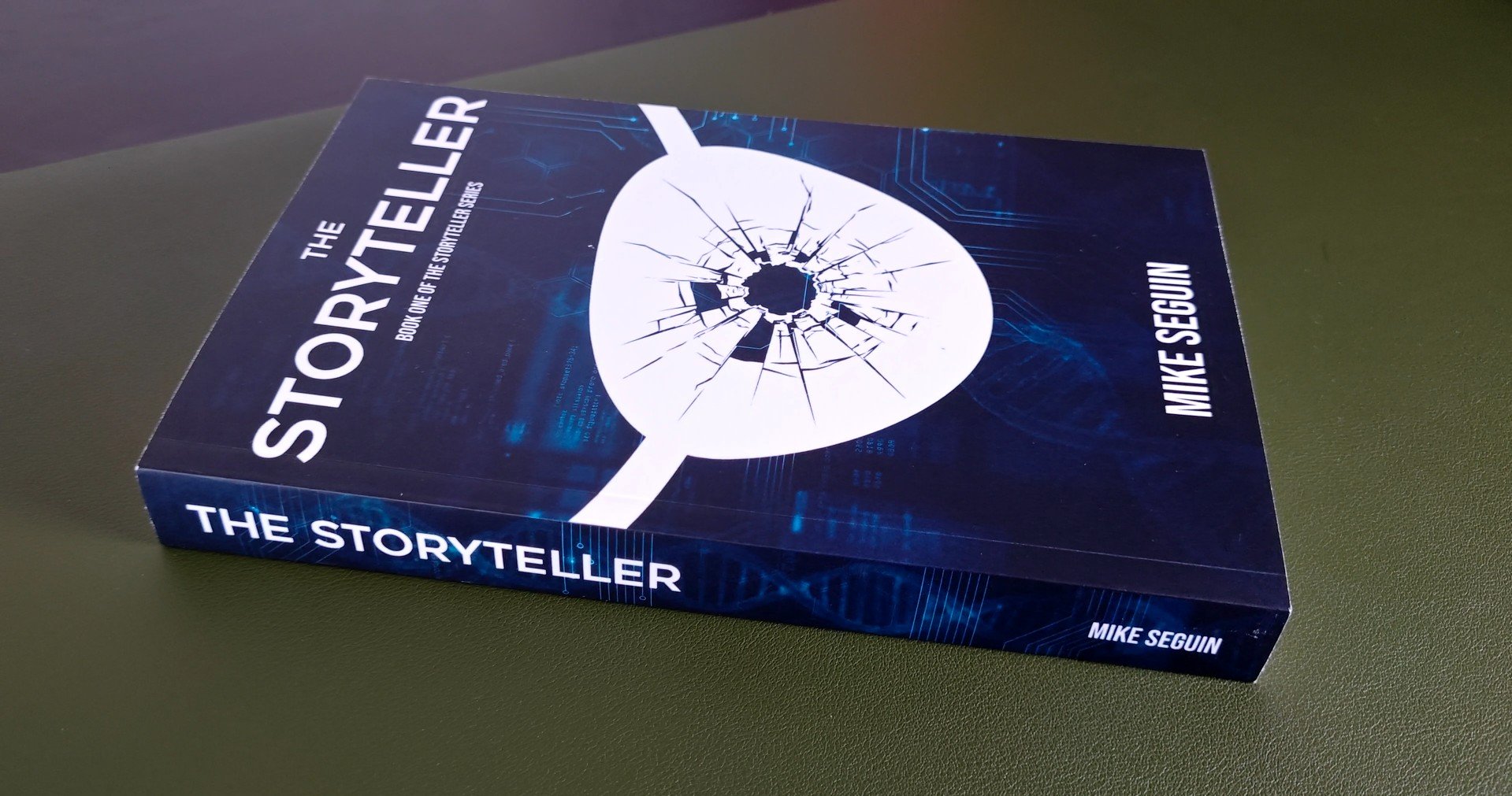 Book titled 'The Storyteller' by Mike Seguin with a cracked eye symbol on the cover, placed on a green surface.