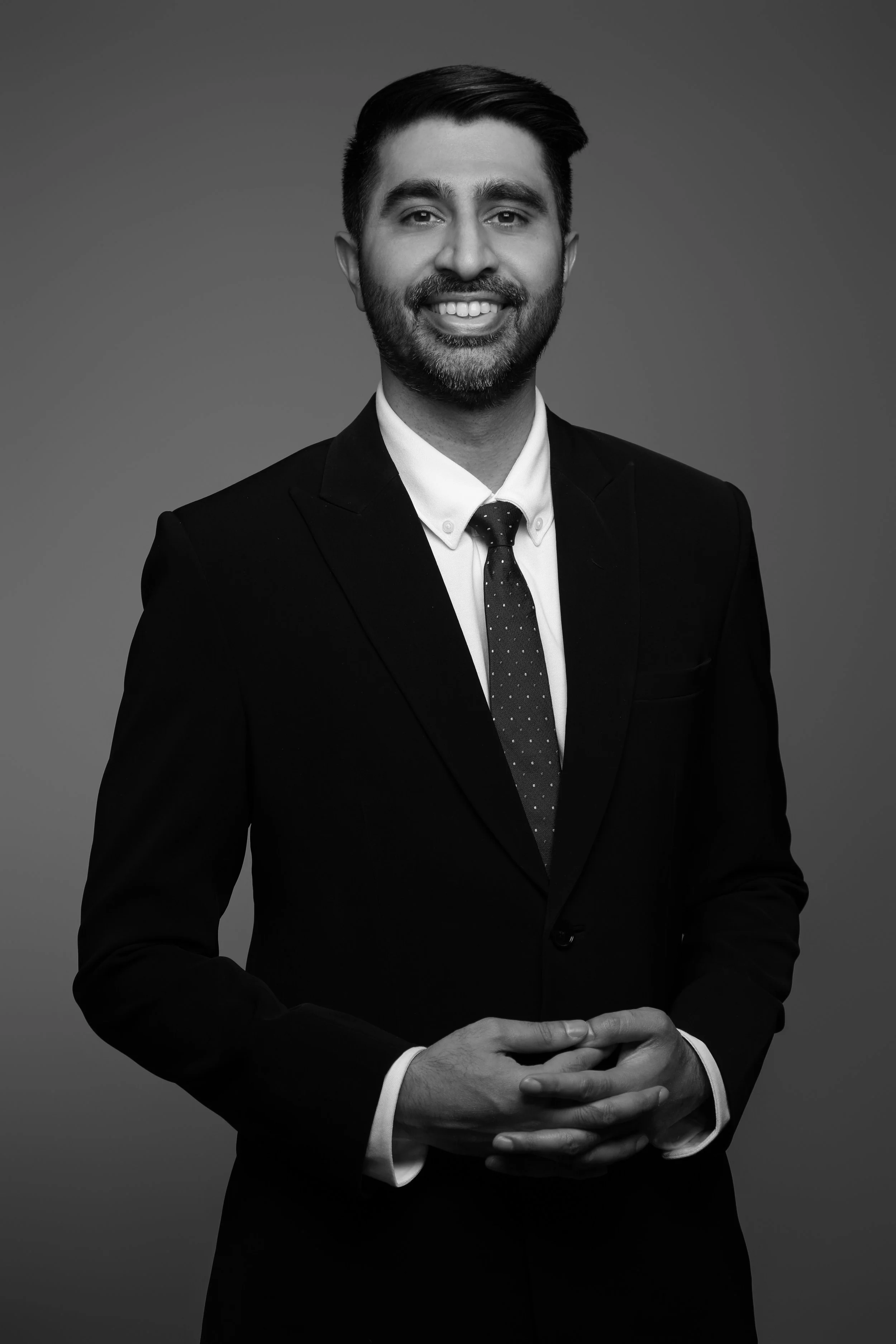 A professional man in a suit smiling and holding his hands together, black and white portrait.
