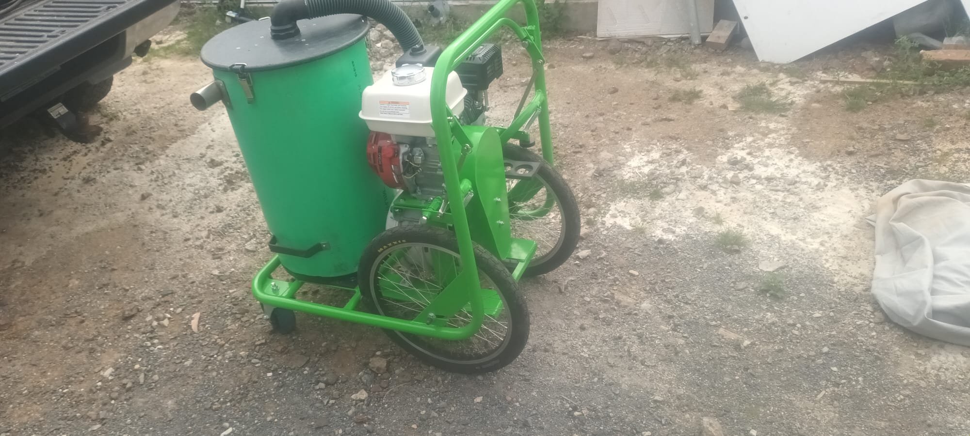 Green portable pressure washer with a hose, engine, and wheels on dirt ground.