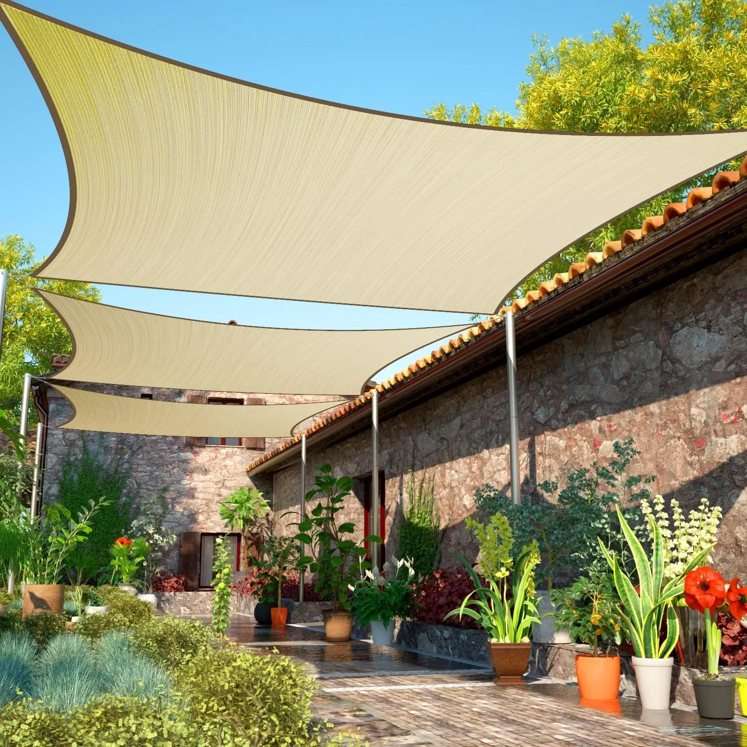 Outdoor patio with hanging beige fabric sun shades, stone wall with window, various potted plants, and lush greenery under a clear blue sky.