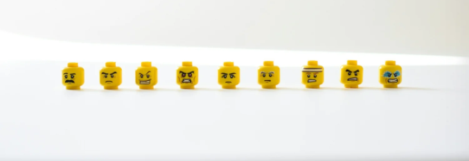 Nine yellow LEGO minifigure heads with various facial expressions lined up on a white surface.