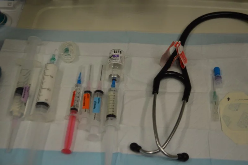 Medical syringes, vials, and a stethoscope arranged on a hospital tray.