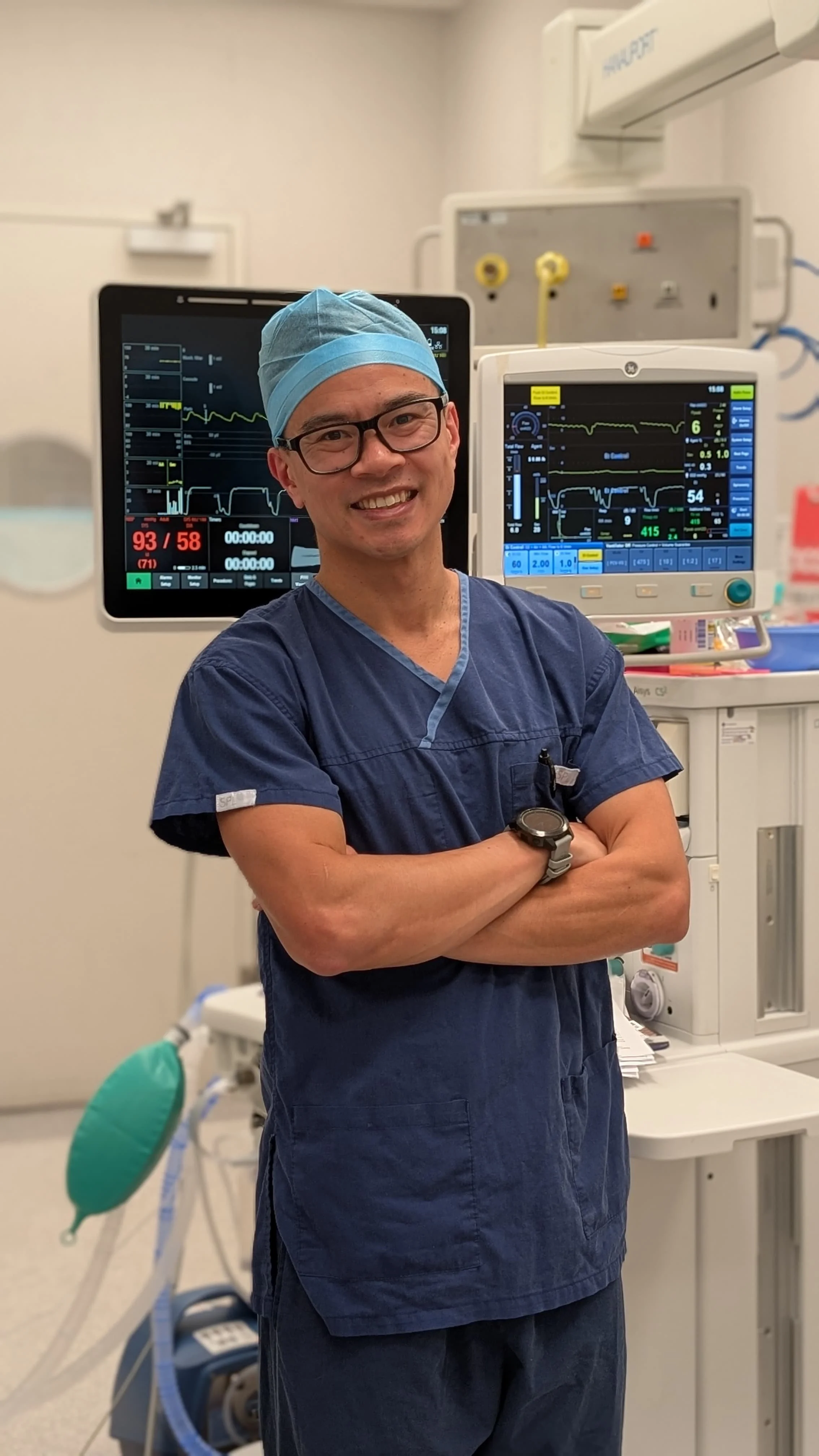Dr Matthew Ho, anaesthetist, stands in front of patient monitoring machines in a hospital operating theatre.