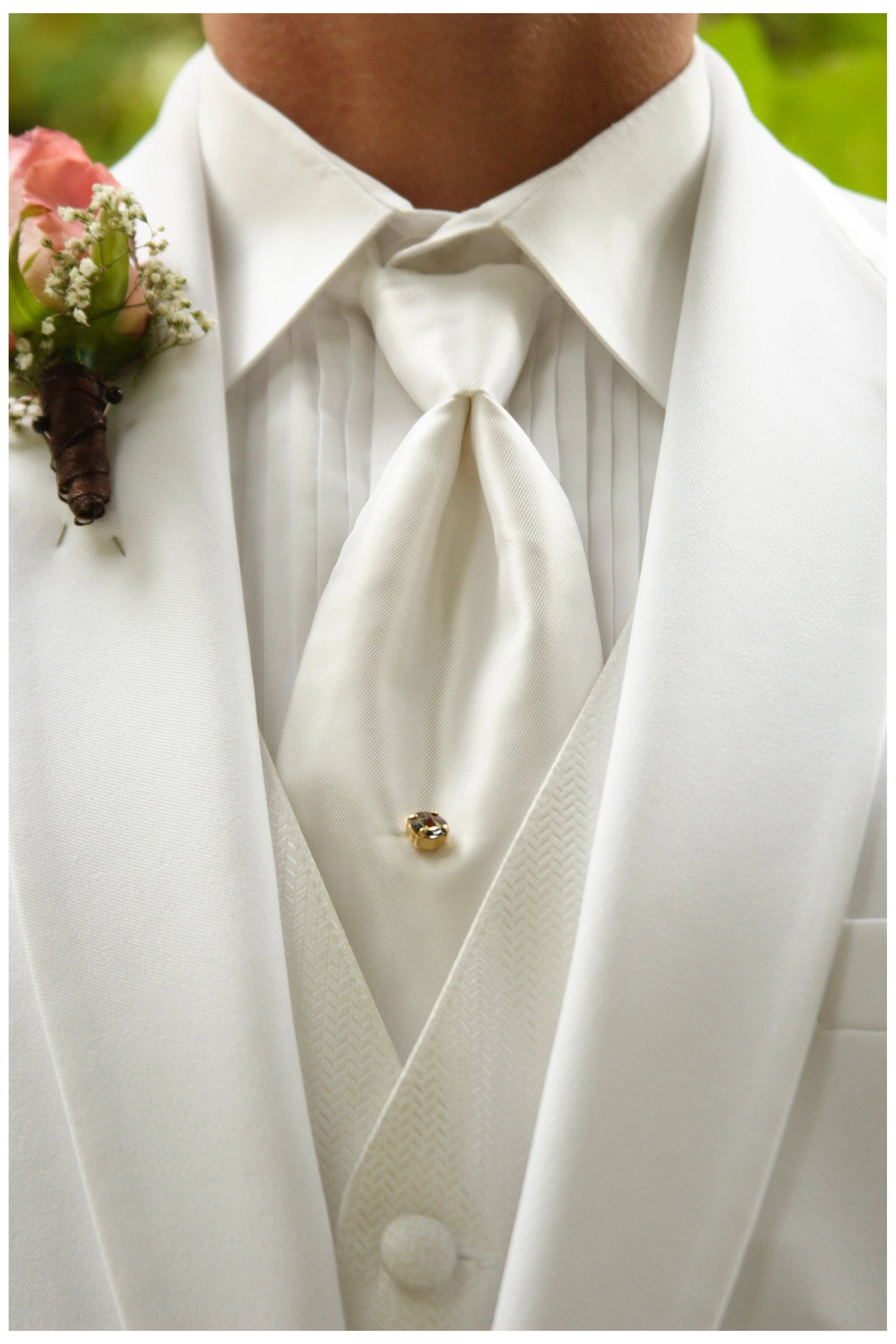 Close-up of a man wearing a white tuxedo with a cravat and gold boutonniere on the lapel.