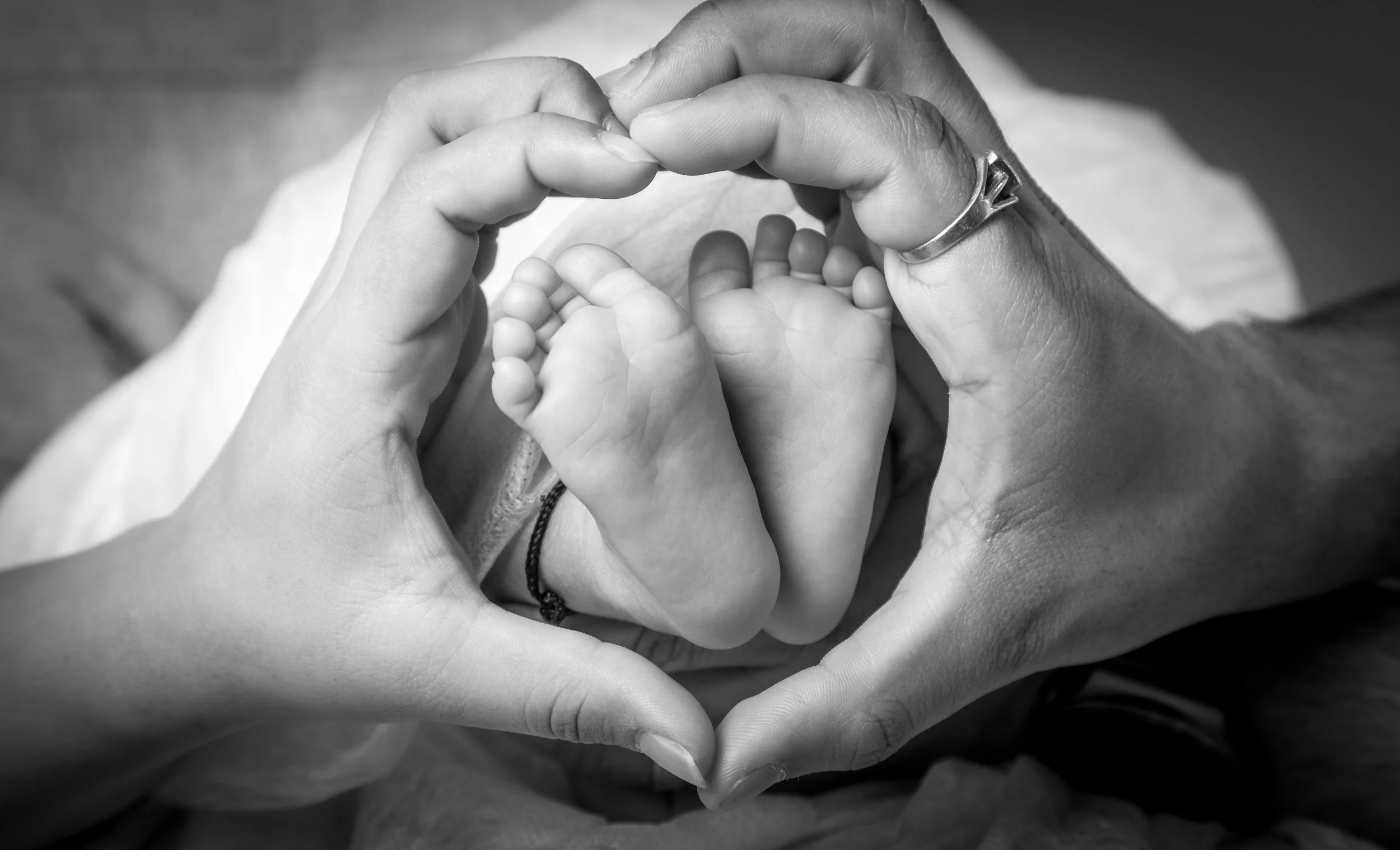Black and white photo of an adult holding a baby's foot, forming a heart shape with their hands.