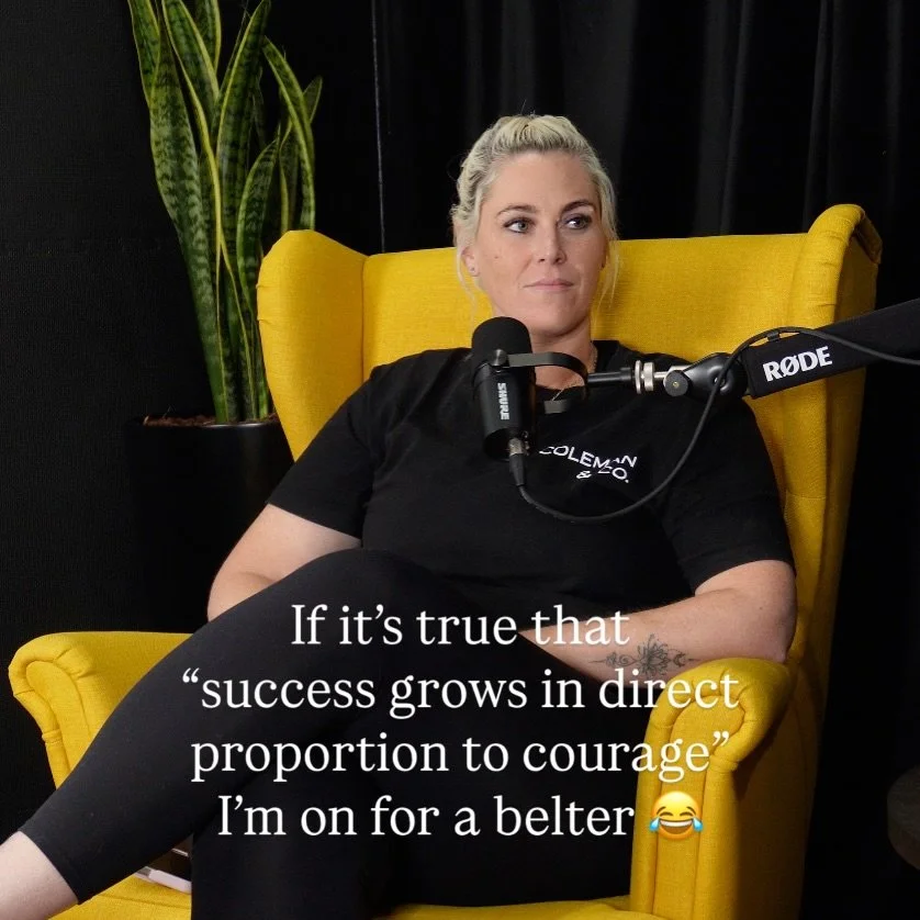 A woman with blonde hair tied back, sitting on a yellow armchair in a podcast studio, speaking into a microphone. She is wearing a black T-shirt and black leggings, with a tattoo on her left forearm. Text overlay says: "If it’s true that success grows in direct proportion to courage I’m on for a belter 😂"