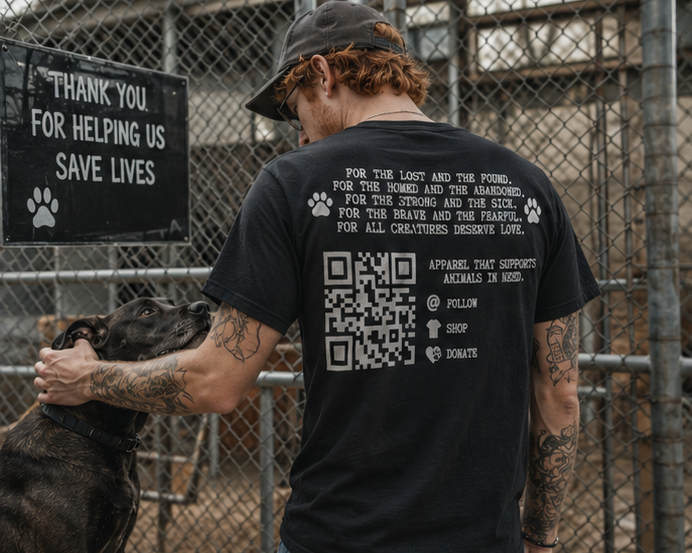 CREATURES supporter with tattoos on his arms and a baseball cap petting a black dog at an animal shelter, with a sign thanking donors for helping save lives.