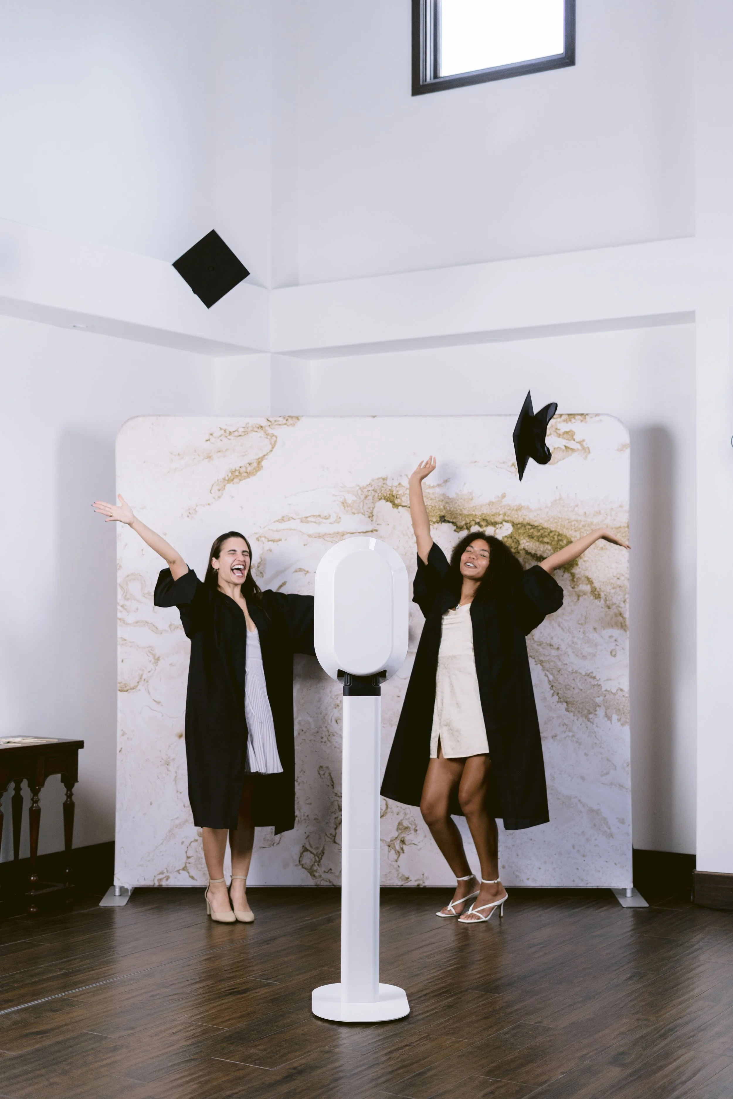 Two guests celebrating beside The 1881 Studio open-air photo booth in a modern marble venue.