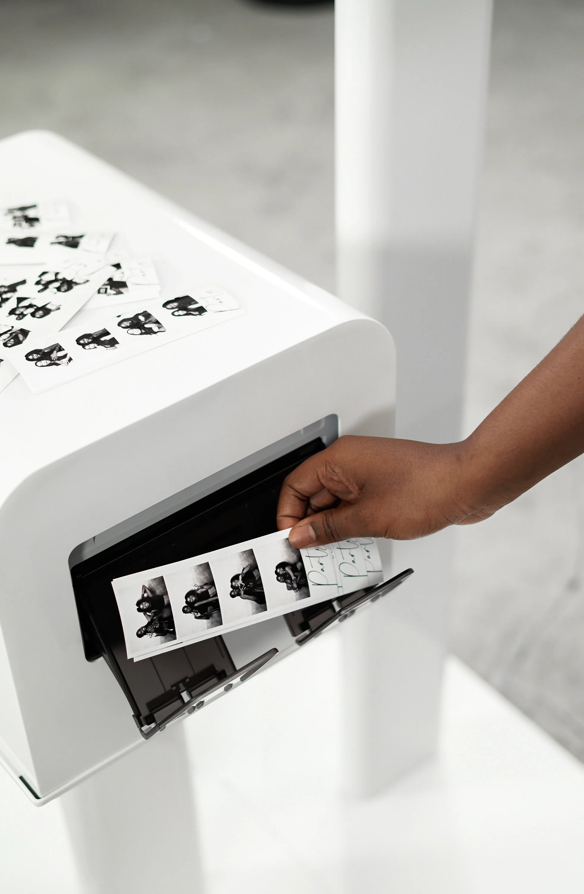 Person pressing a button on a printer, with photo strips from The 1881 Studio photo booth print station.