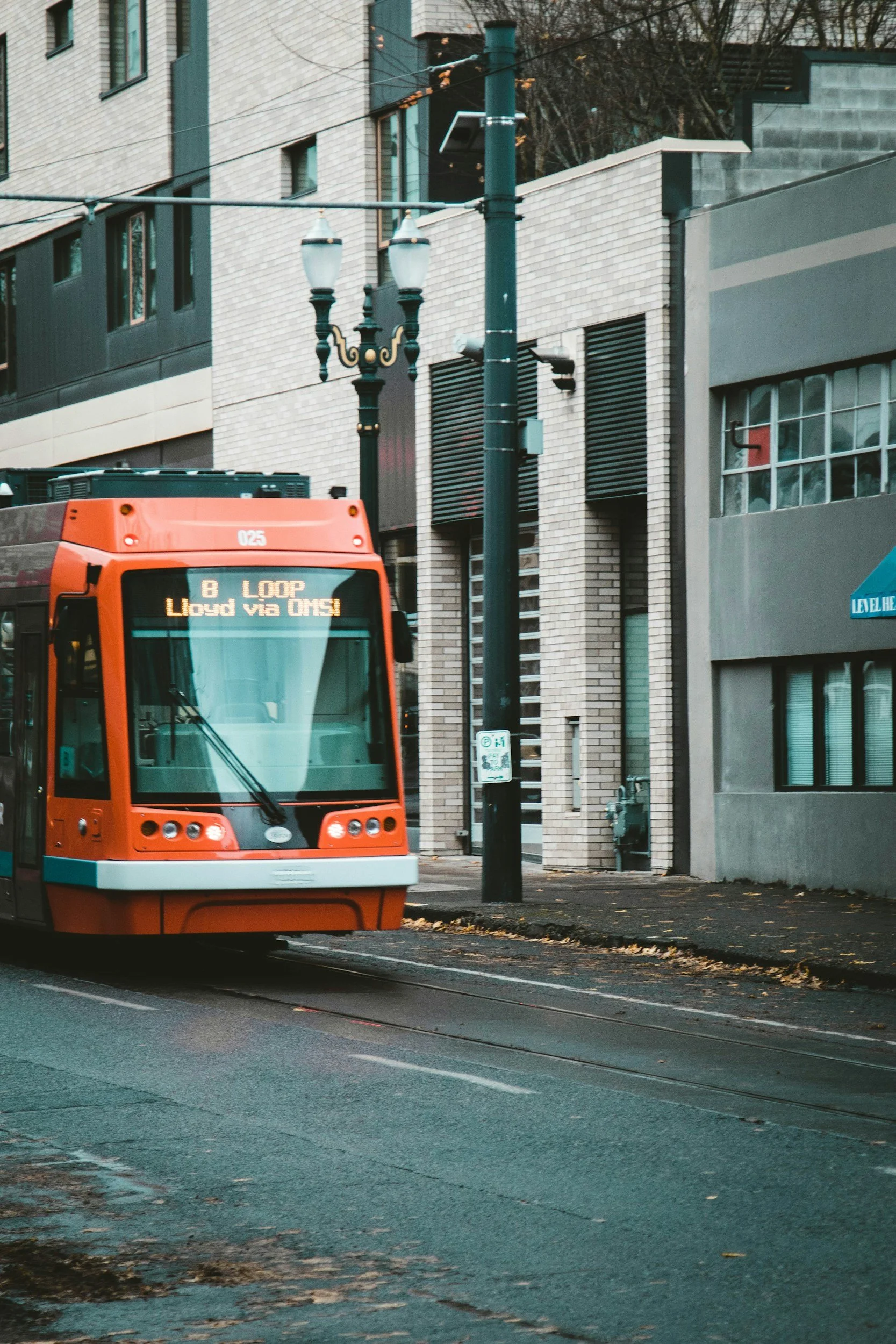 An orange streetcar with electronic destination sign reading 'B LOOP Lloyd via OMS' on a city street, with modern buildings and streetlights in the background.