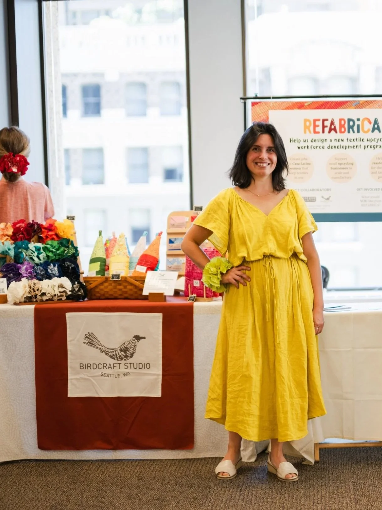Birdcraft Studio founder, Gabriela Faundez, at a Seattle craft market table with her small-batch handmade upcycled accessories, reclaimed-fabric goods, and a ReFabrica textile reuse display.