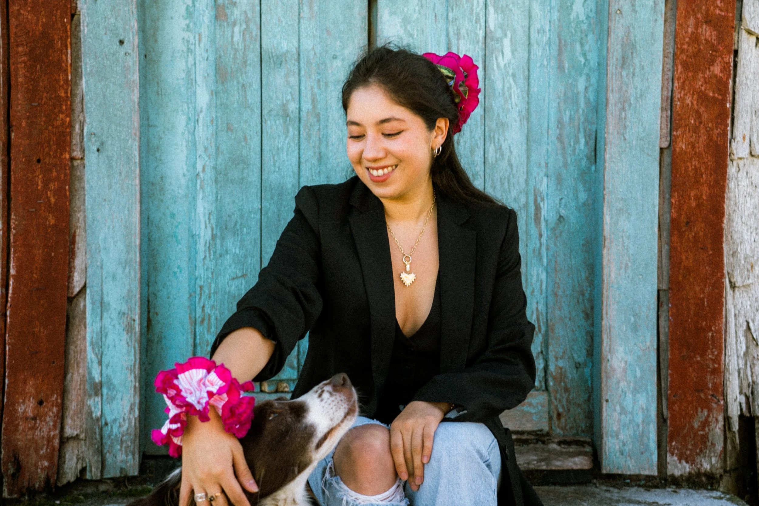 Birdcraft Studio ruffled scrunchies made from reclaimed fabric are styled in a woman’s hair and on her wrist while she pets a small dog.