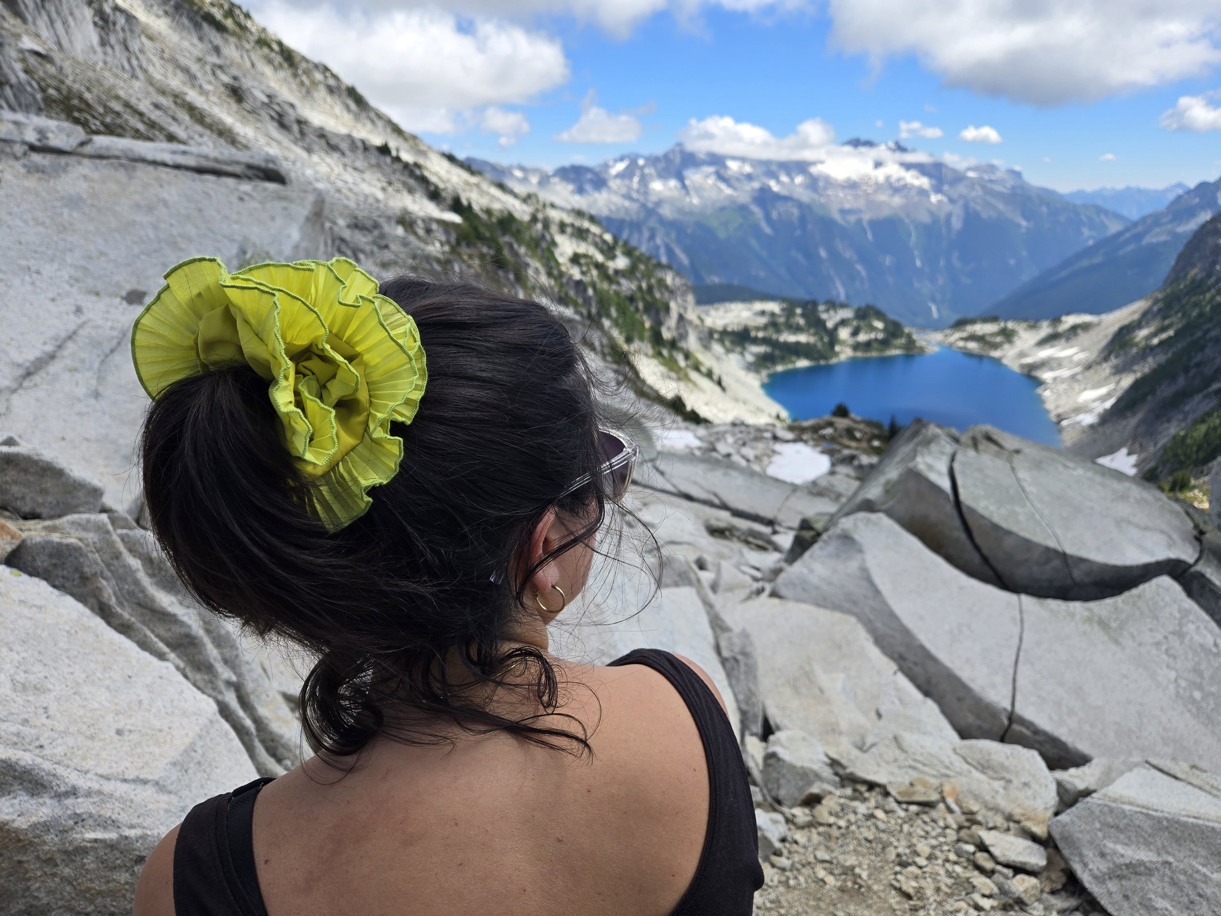 Yellow ruffled upcycled scrunchie by Birdcraft Studio, made from upcycled fabric and worn outdoors by a young women, near an alpine lake in the Cascade mountains, Washington state.