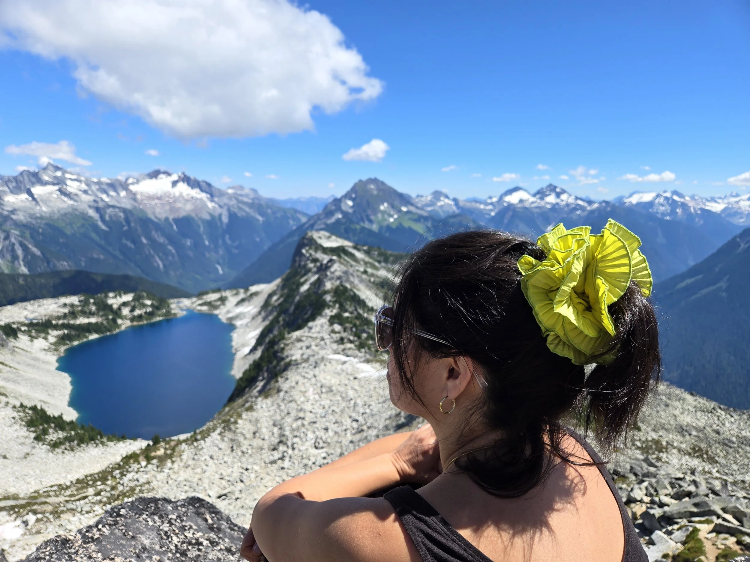 Yellow ruffled upcycled scrunchie by Birdcraft Studio, made from reclaimed fabric and worn outdoors by a young women, near an alpine lake in the mountains.