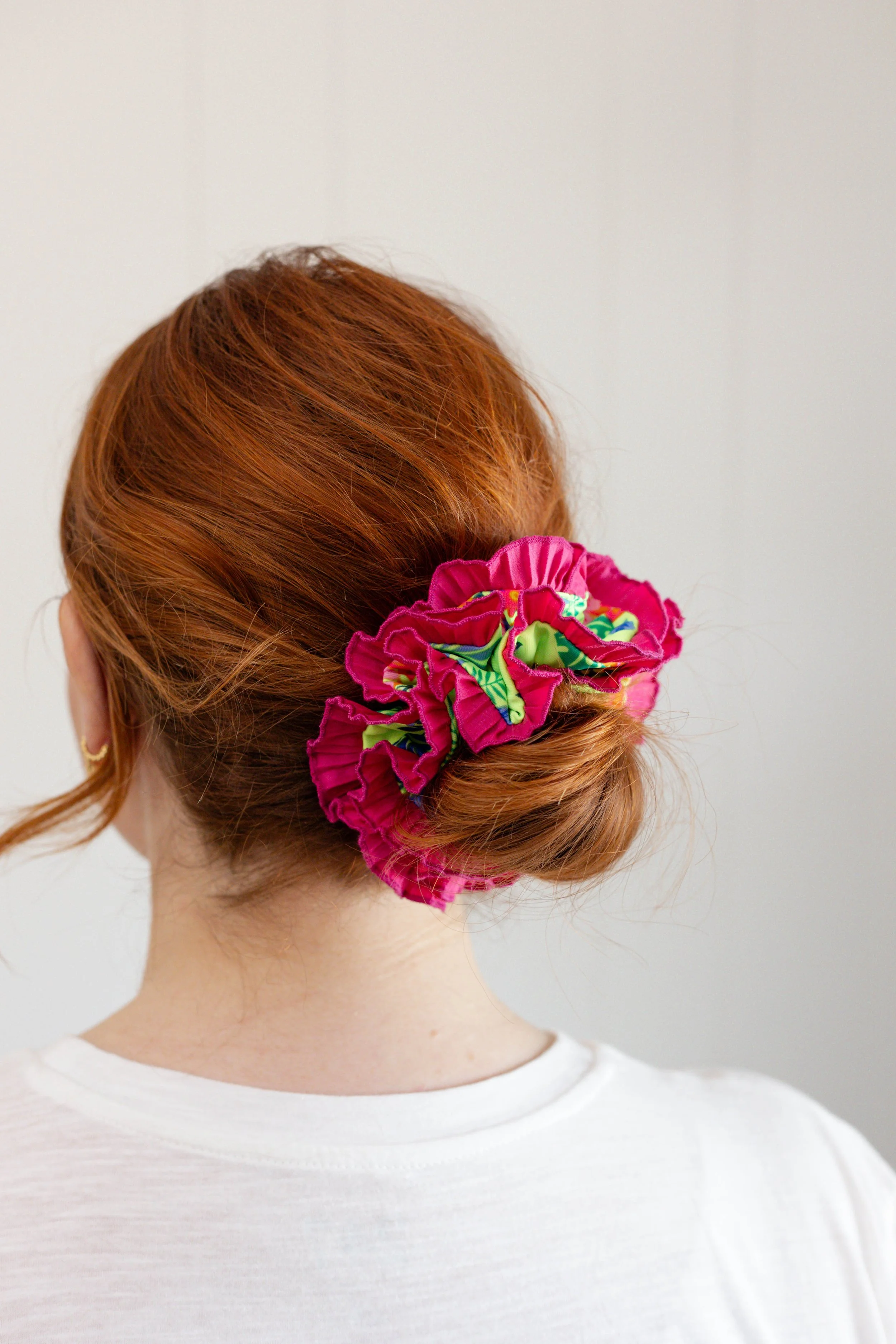 Back view of a woman with red hair wearing a neon pink Birdcraft Studio ruffled scrunchie made from reclaimed fabric.