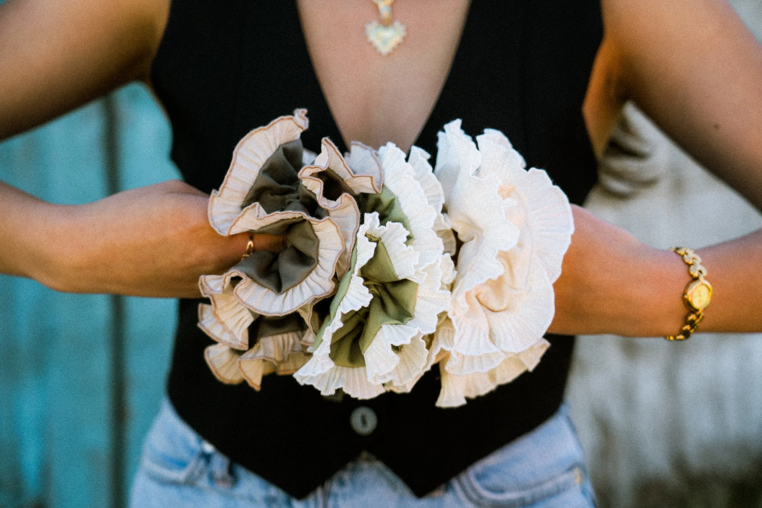 A woman holds a set of three colorful ruffled scrunchies by Birdcraft Studio, handmade from reclaimed fabrics and designed as small-batch upcycled accessories