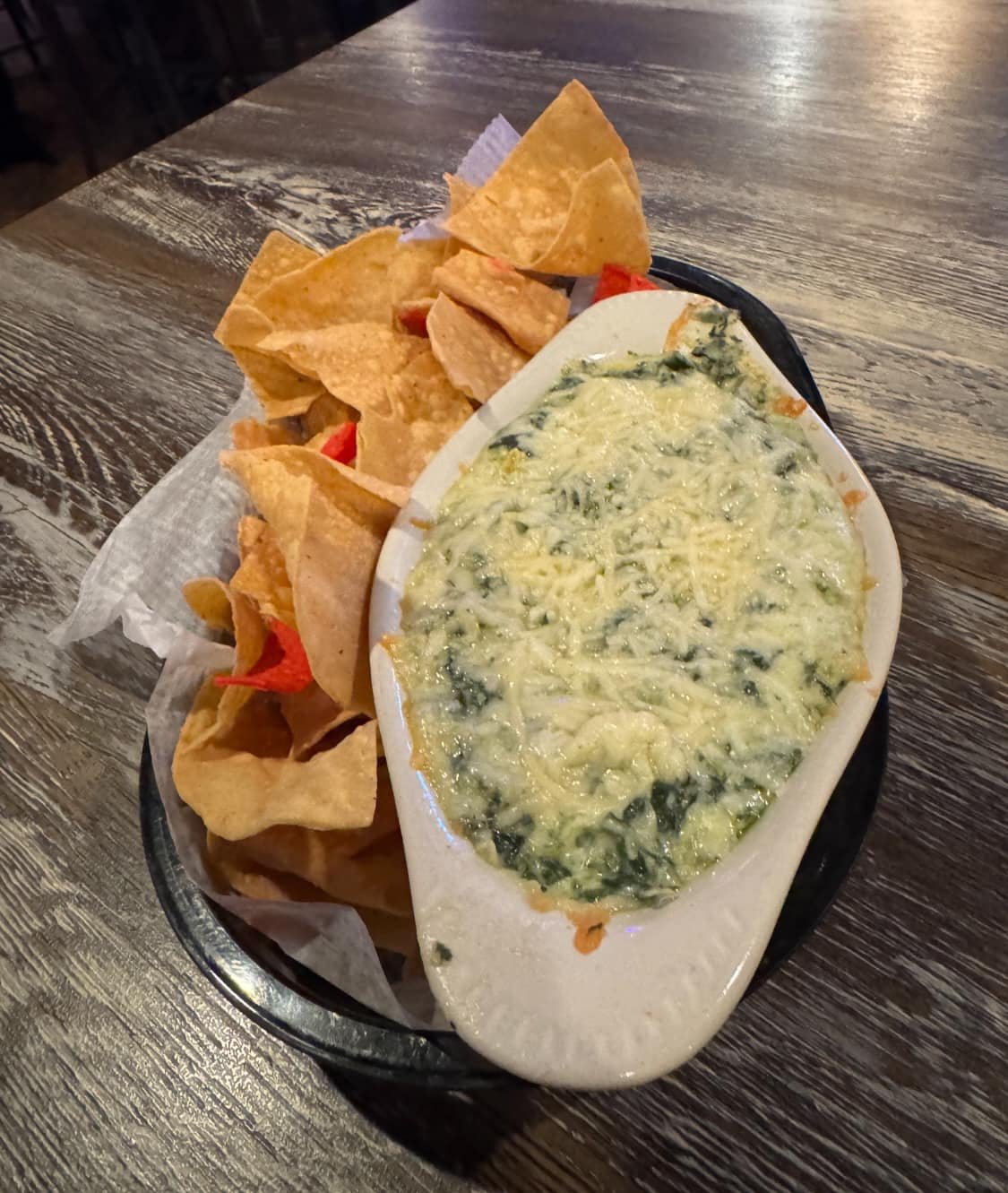 A plate of spinach artichoke dip with tortilla chips on a wooden table.