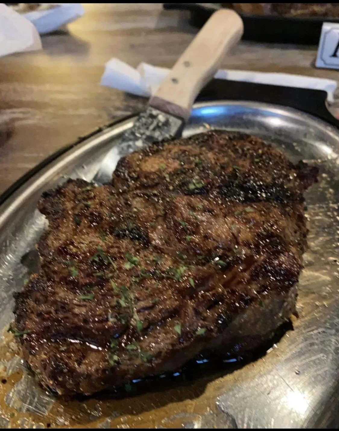 A cooked prime rib roast with a browned, seasoned crust served on a metal platter, with a carving knife resting on the side.