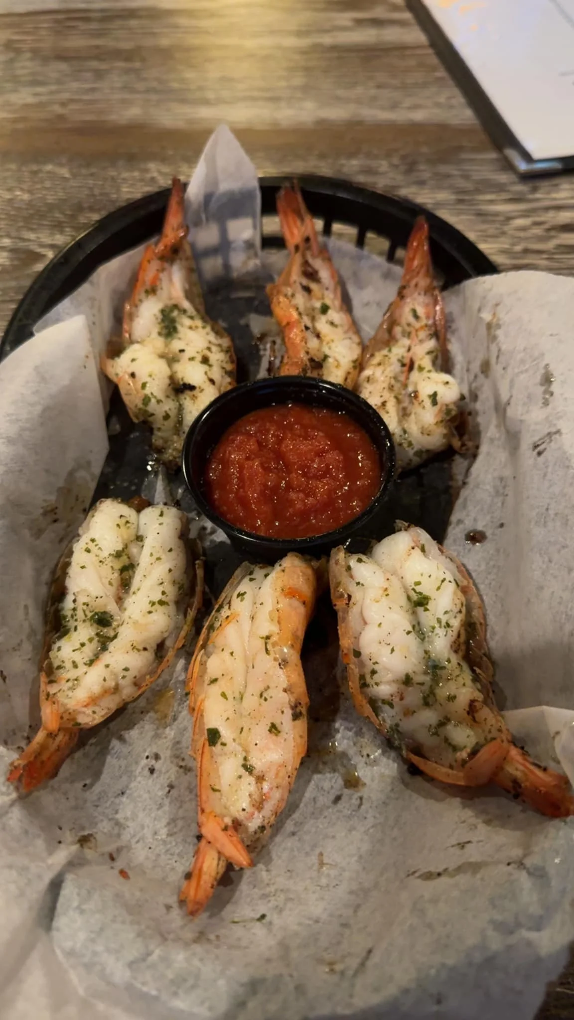 Grilled shrimp with herbs served with a side of red dipping sauce, arranged on parchment paper in a basket.