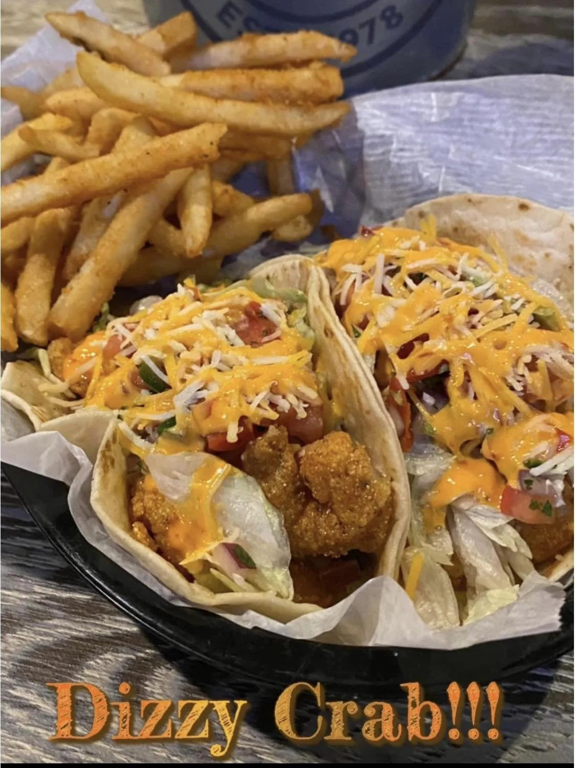 Three tacos filled with fried crab, lettuce, tomato, shredded cheese, and sauce, served with a side of French fries.